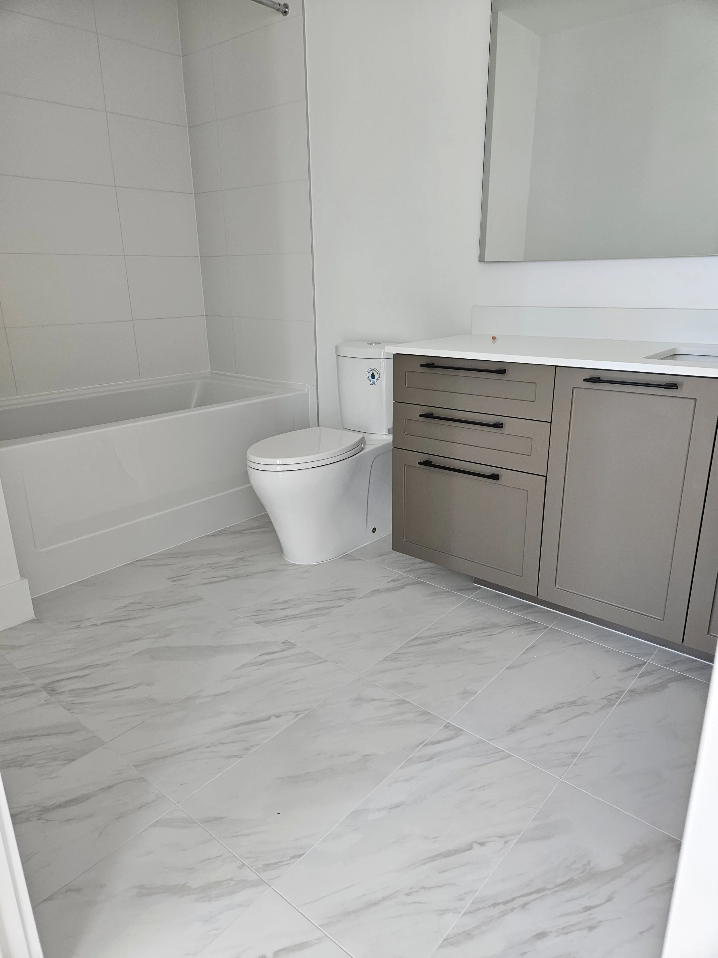 A modern bathroom with a bathtub, a white toilet, and a vanity with drawers and a large mirror above.