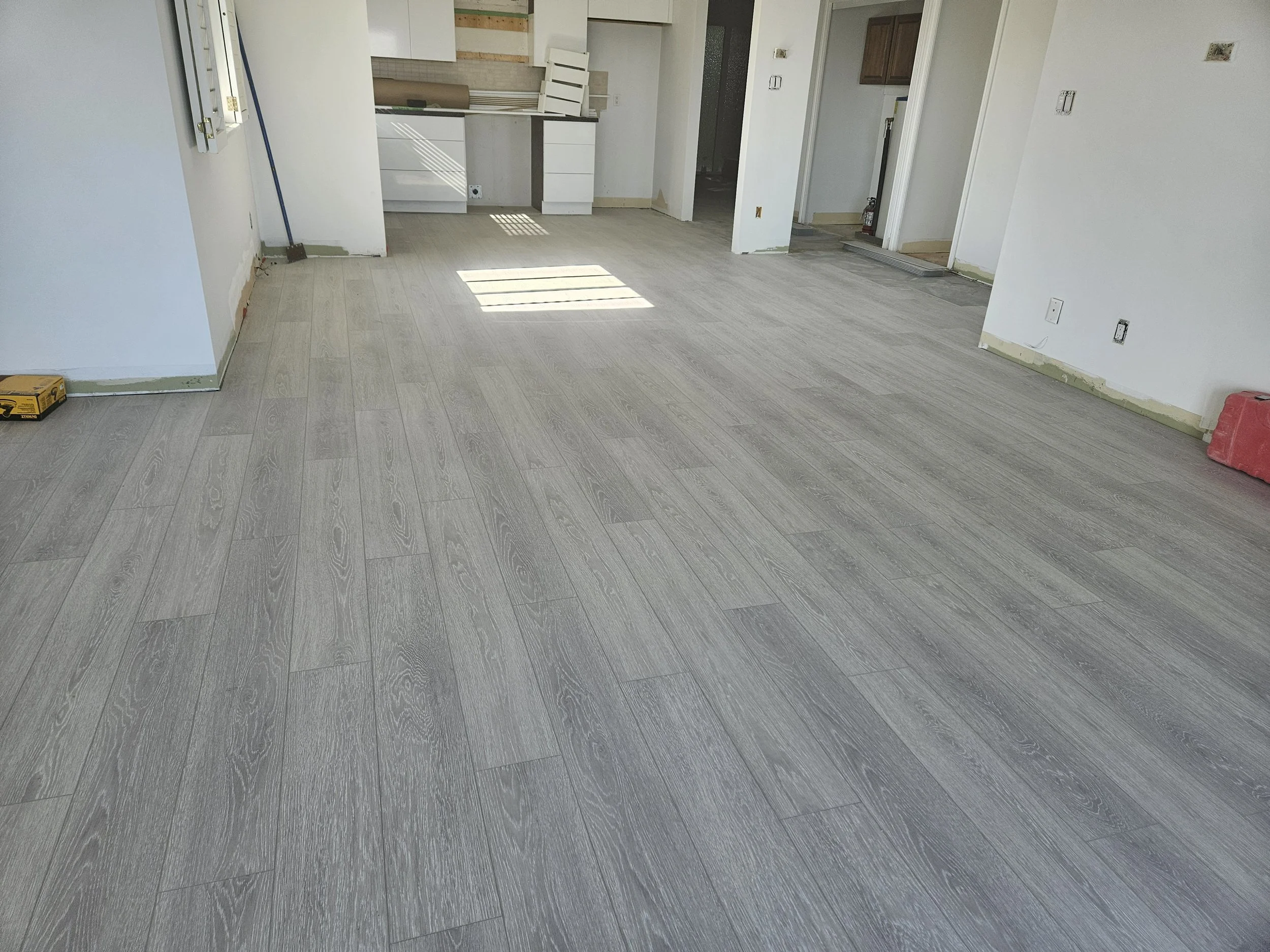 Room under construction with newly installed wood-look flooring, unpainted walls, and construction tools.