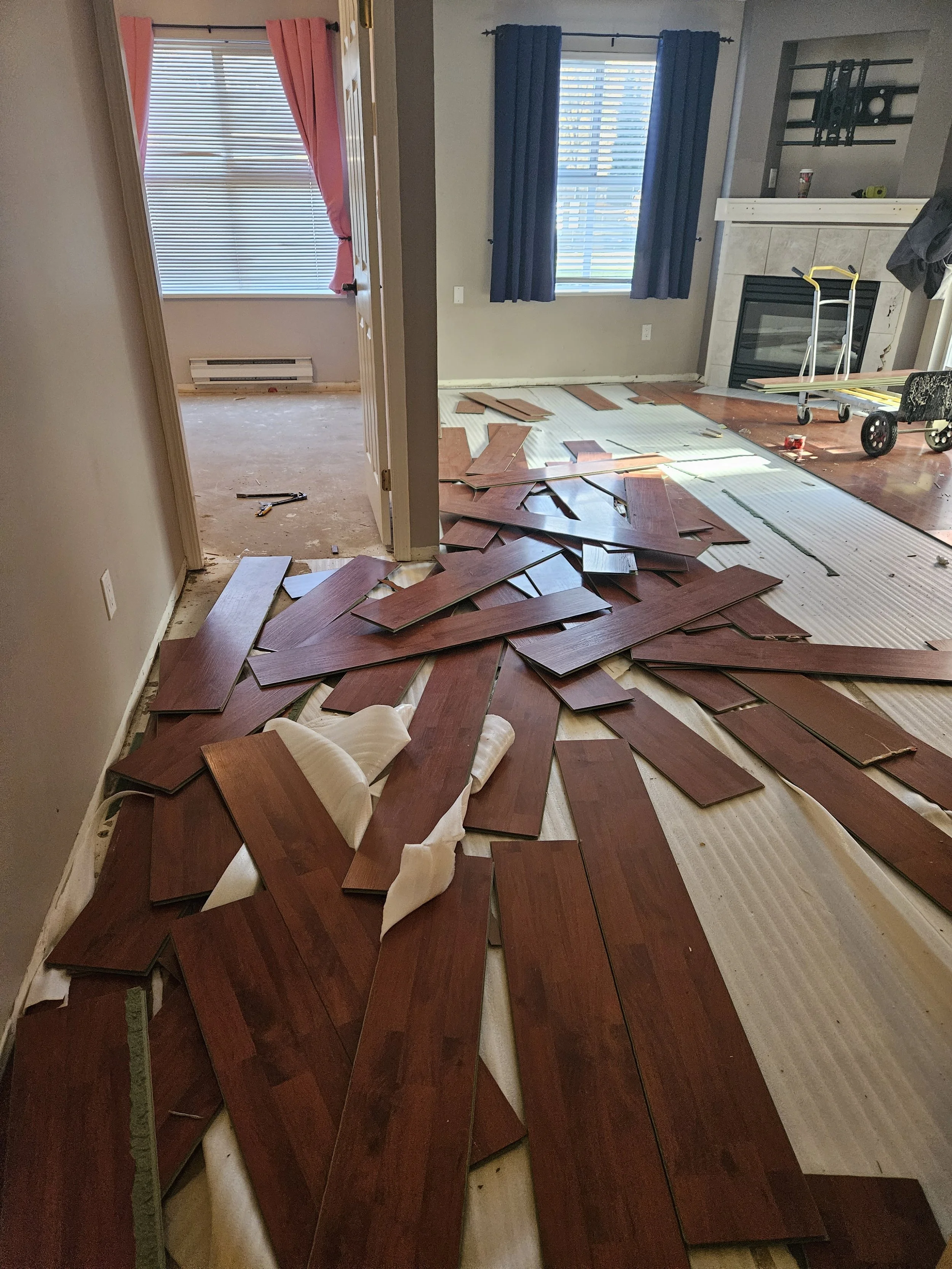 Living room with scattered wooden flooring planks, some partially installed, and construction tools.