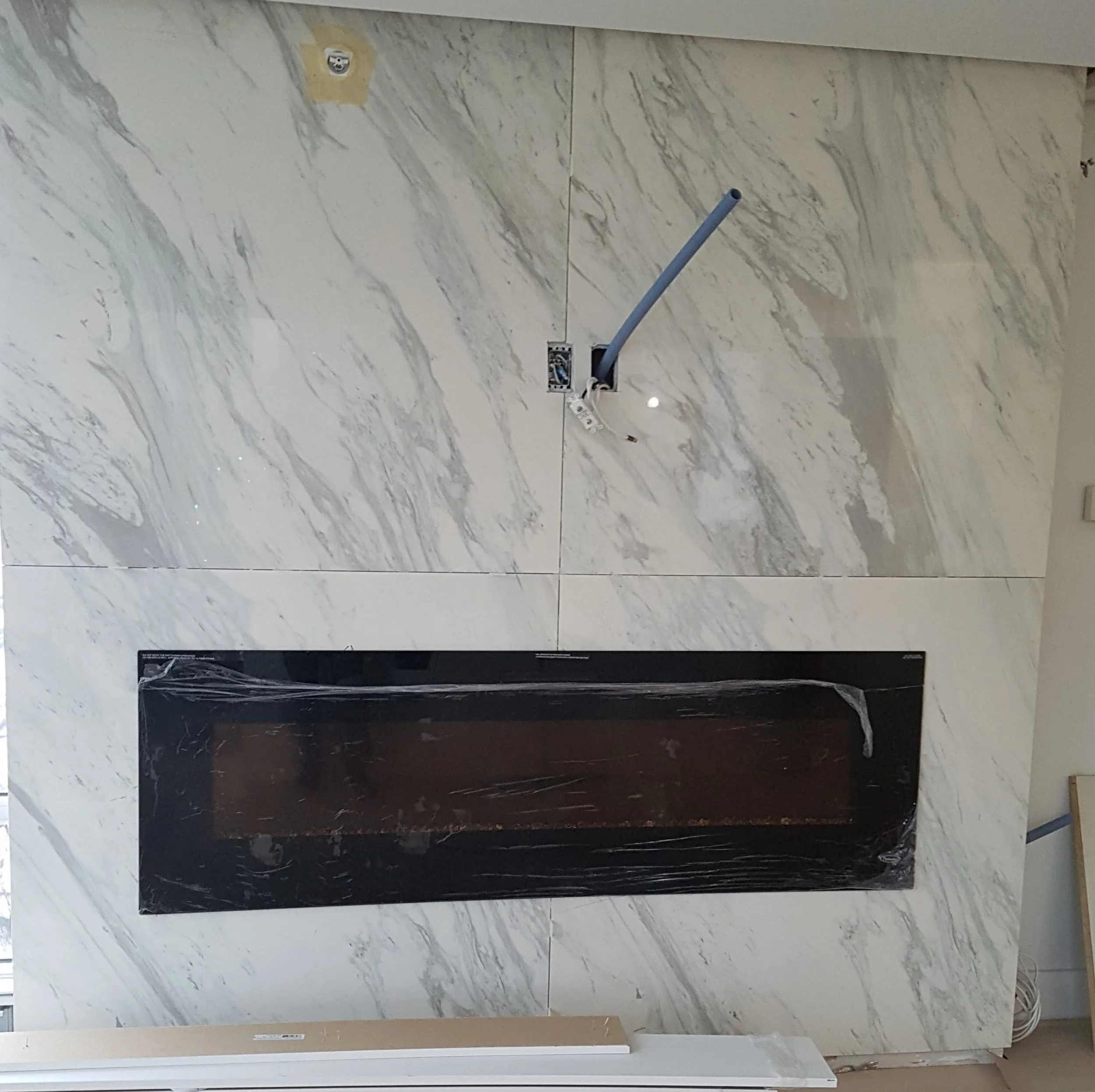 Marble wall with a blue electrical conduit pipe and a black rectangular frame covered with plastic wrap.