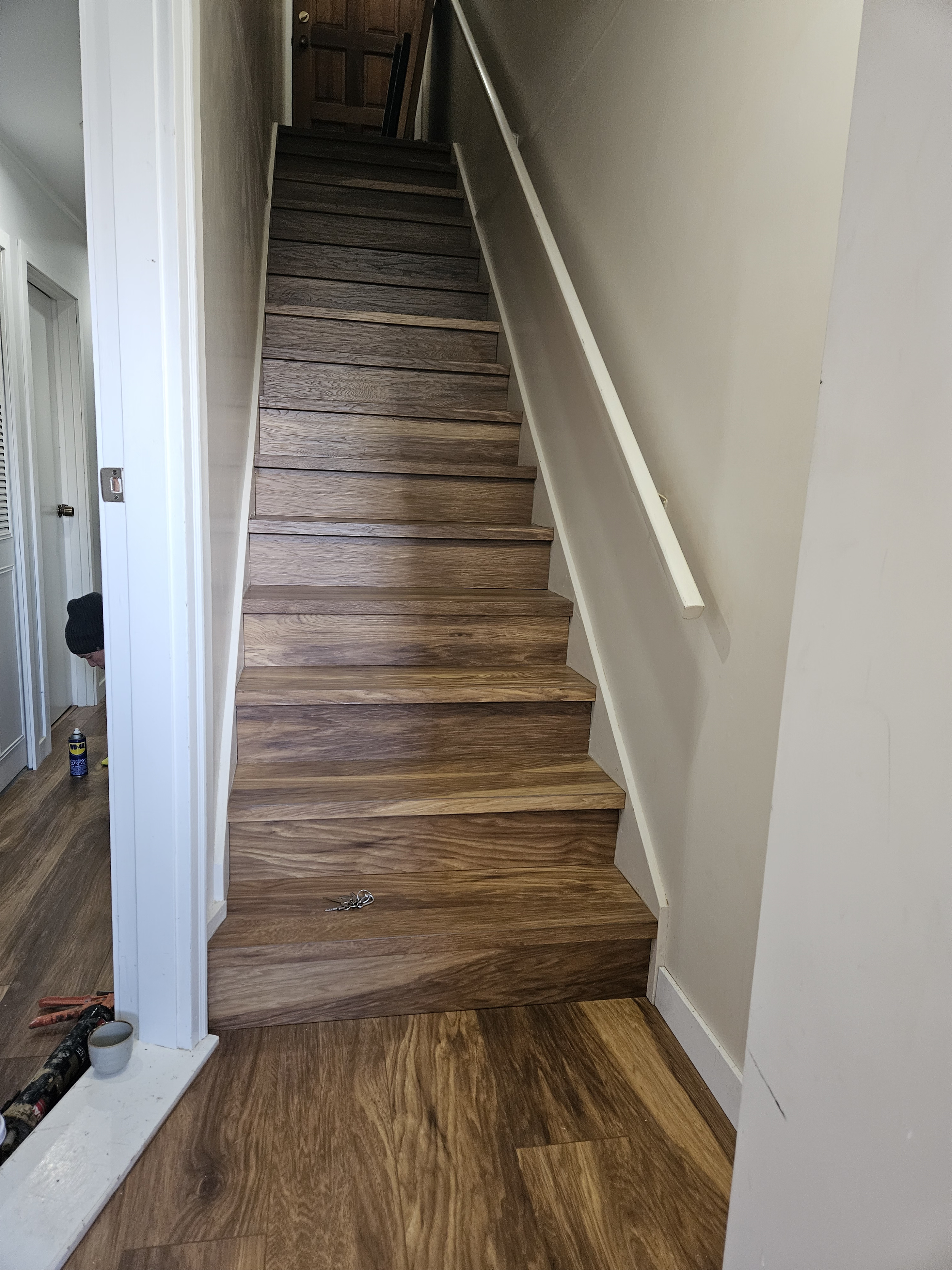 Newly installed wooden staircase with white handrail in a home interior, with unfinished section and construction tools visible at the bottom.