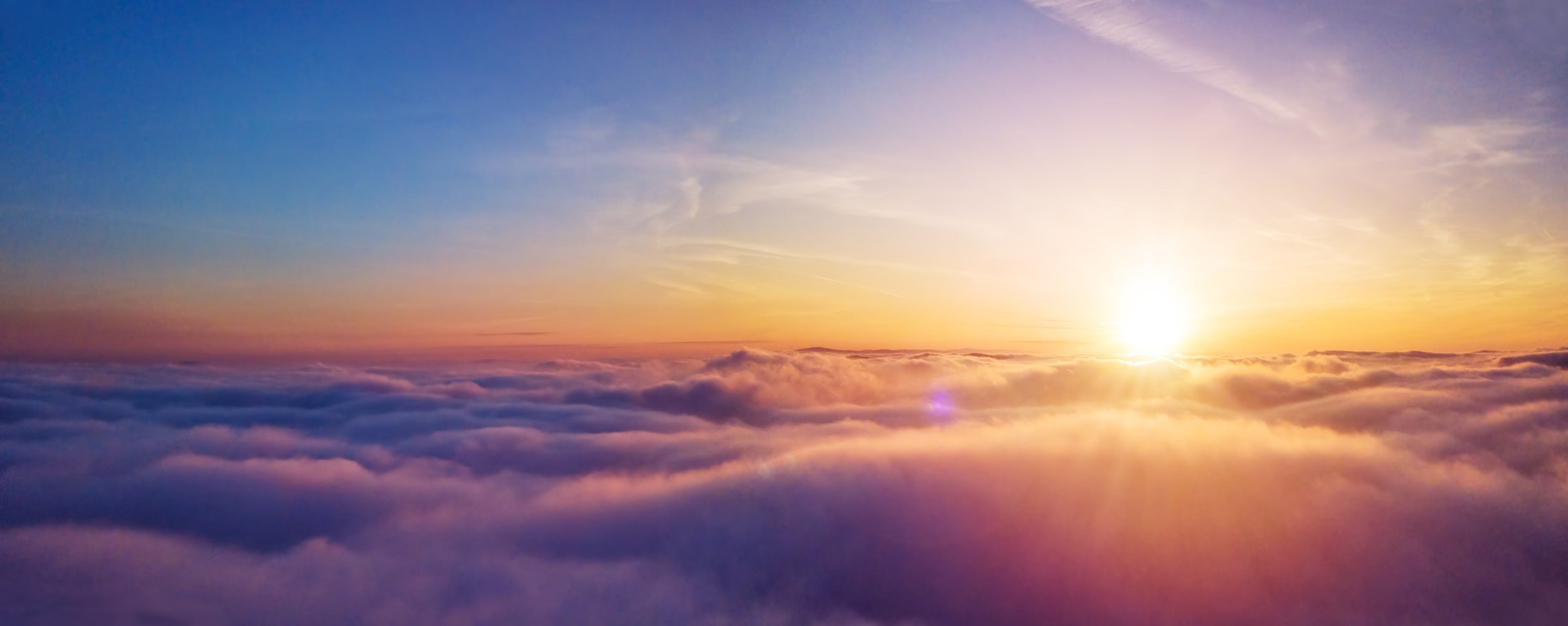 Sunrise over a sea of clouds, with a gradient sky transitioning from blue to pink and orange.
