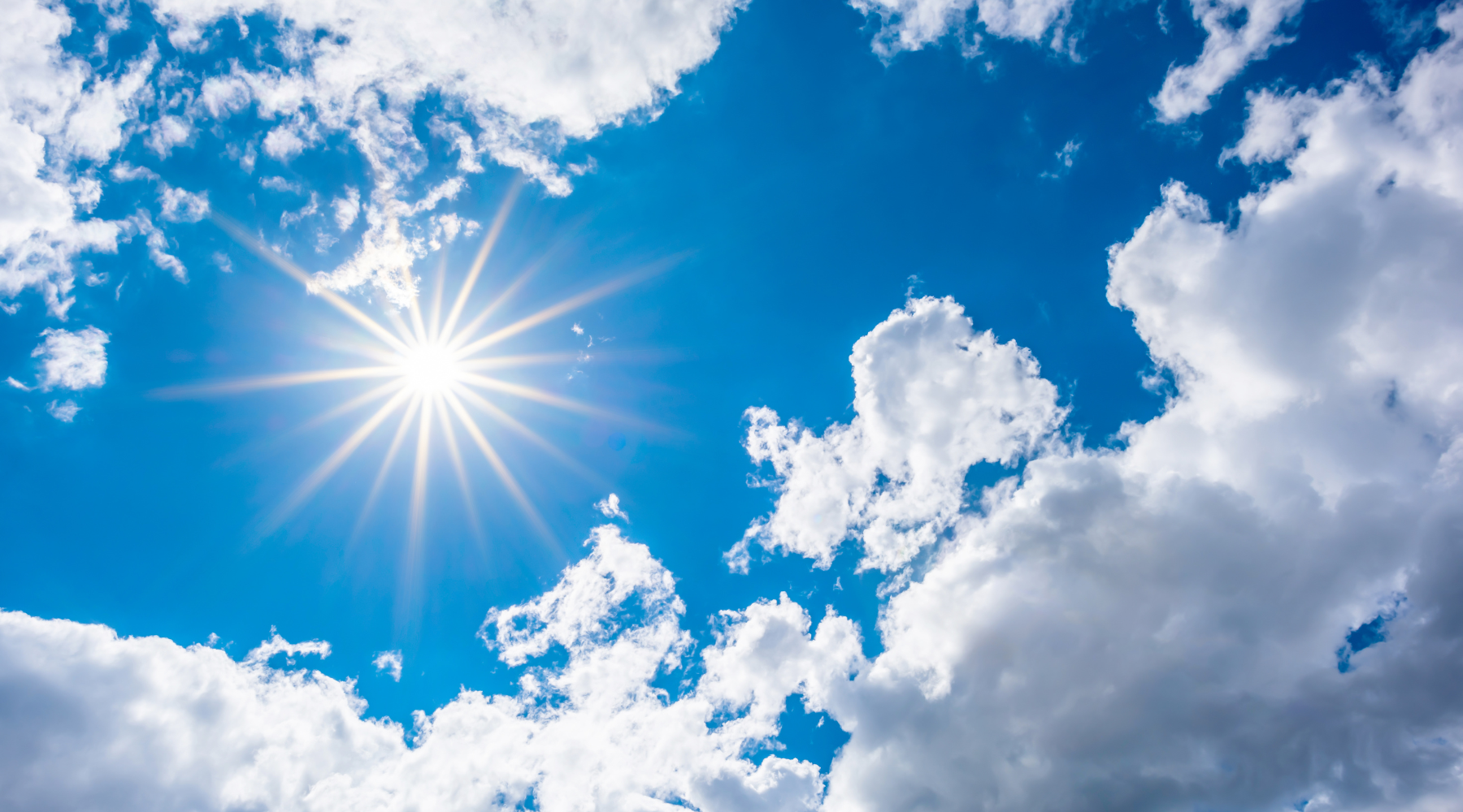 Bright sun shining through white clouds in a blue sky.