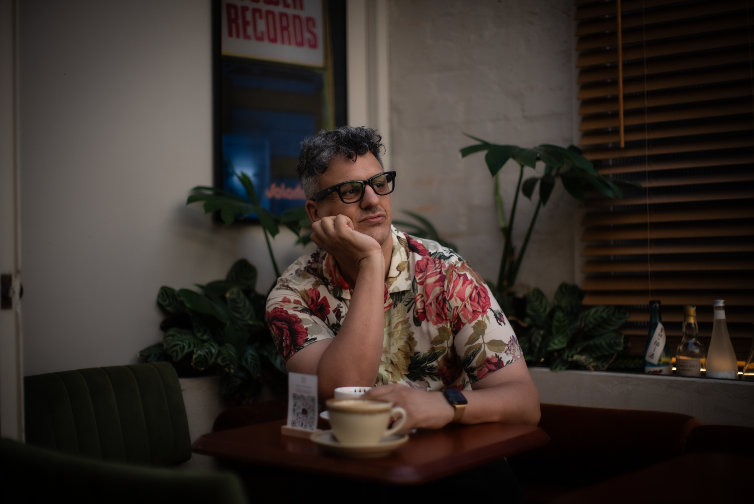 A man holding a coffee and leaning his face onto his other hand starting into the distance