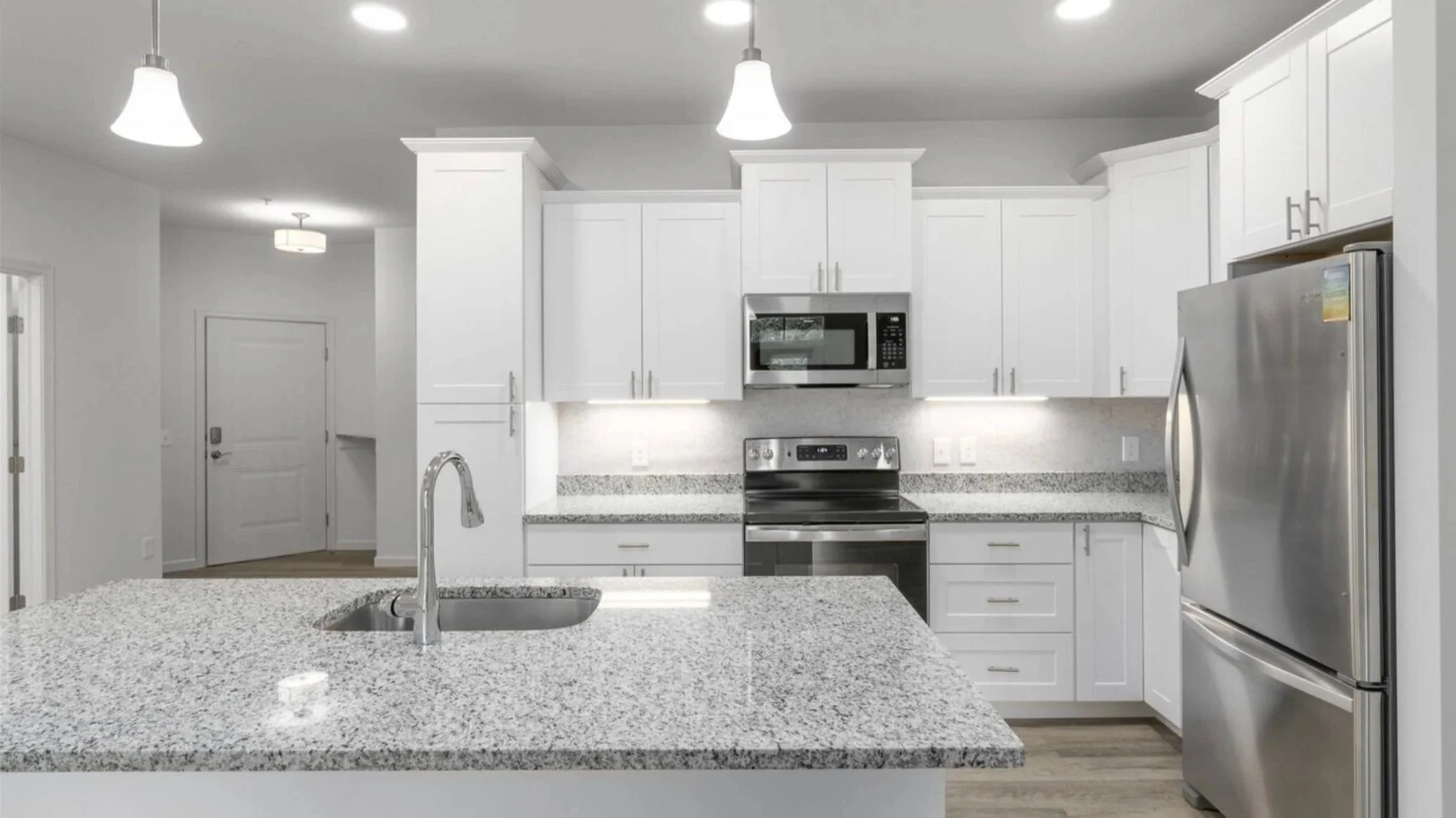 Modern kitchen with white cabinets, stainless steel appliances, and granite countertops. Includes a sink in the foreground and ceiling lights.