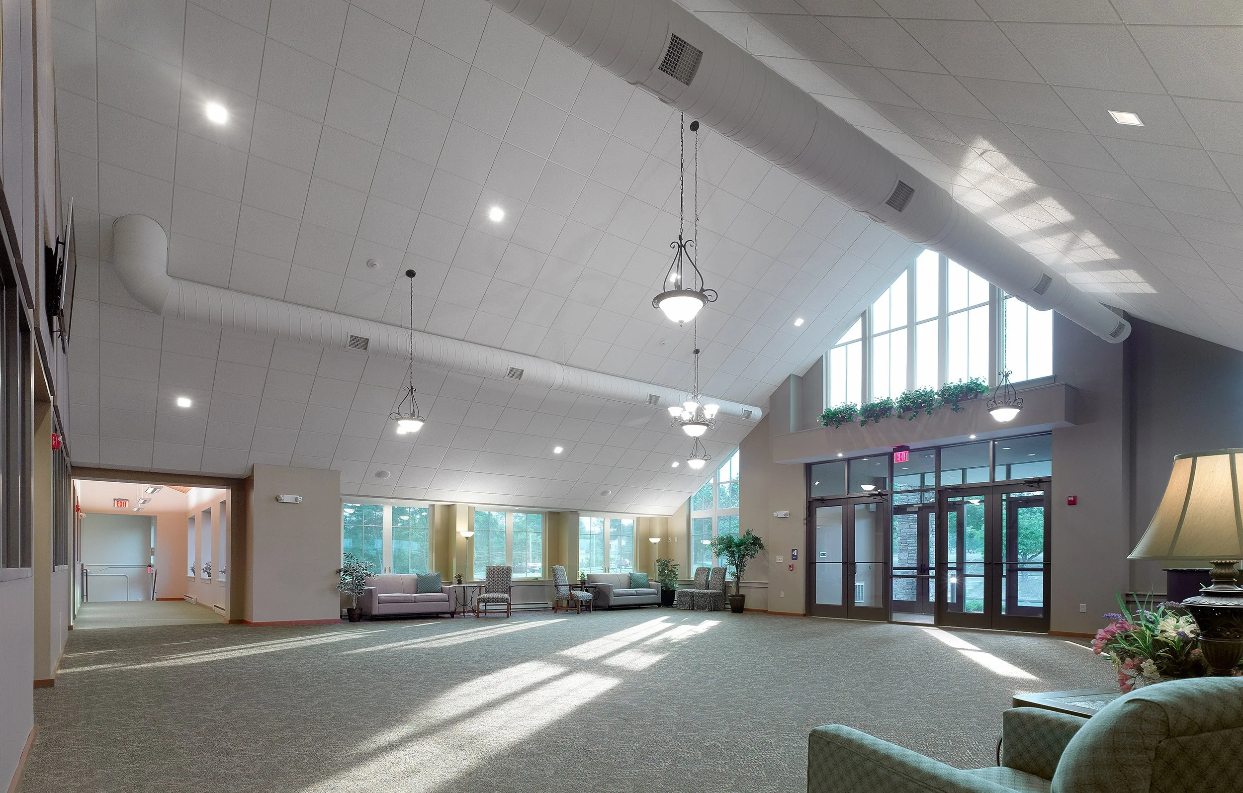 Interior view of a spacious, well-lit church narthex with high ceiling, large windows, and modern furnishings including sofas and plants.