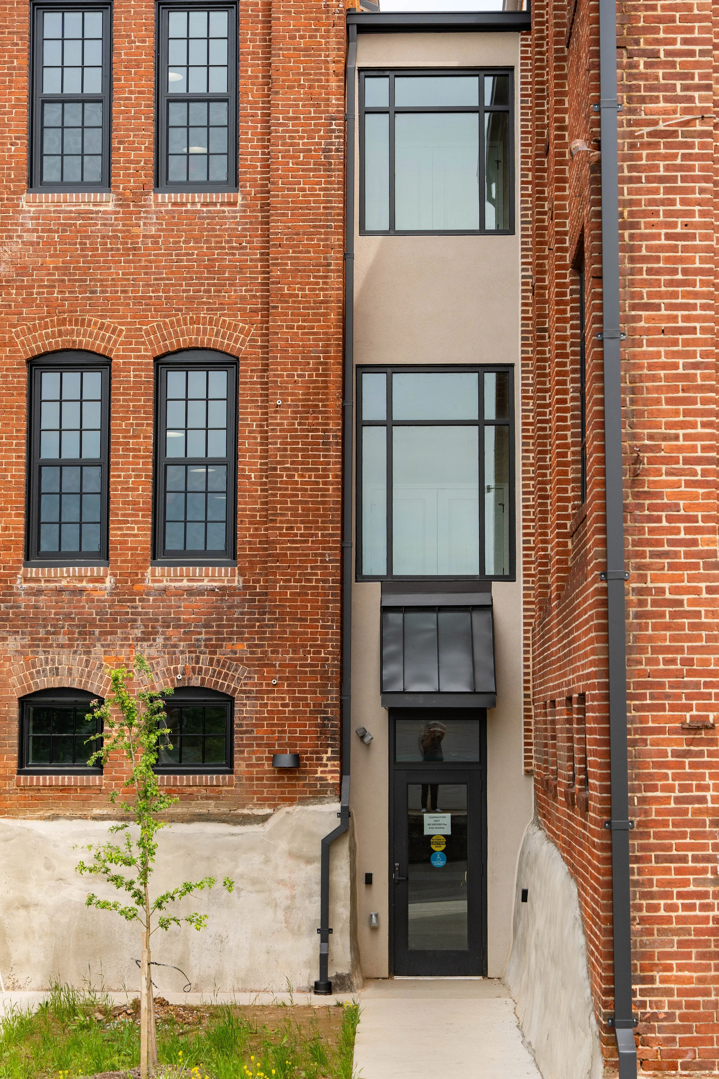Apartment building with a brick facade, black-framed windows, and a gray entrance door with a small awning.
