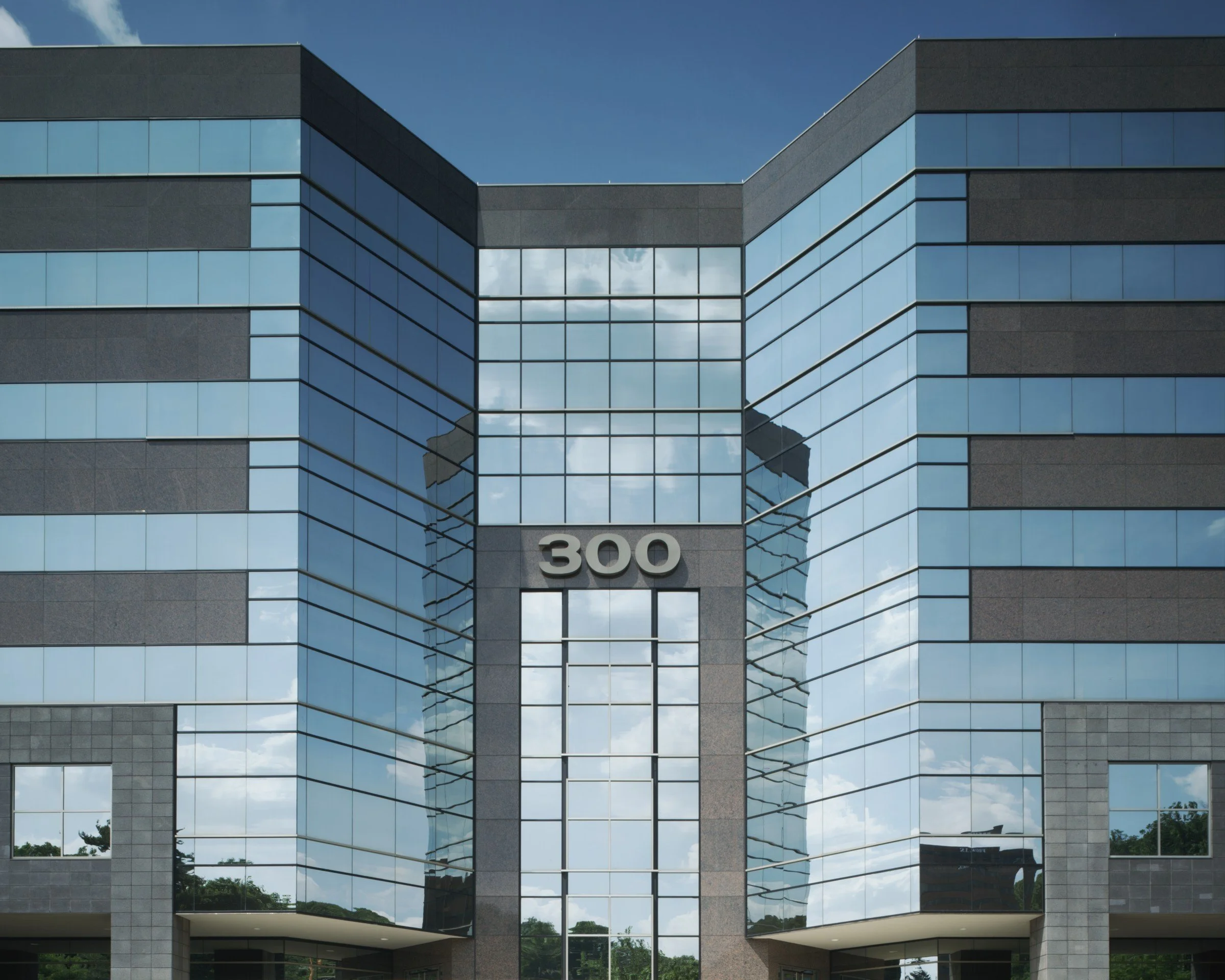 Reflective glass windows on a modern office building with the number 300 displayed at the entrance.