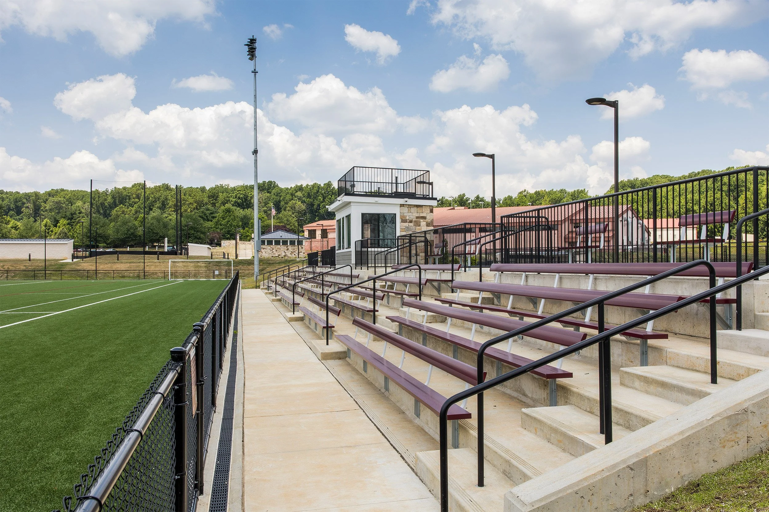 Empty bleacher seats at a sports field under a partly cloudy sky.