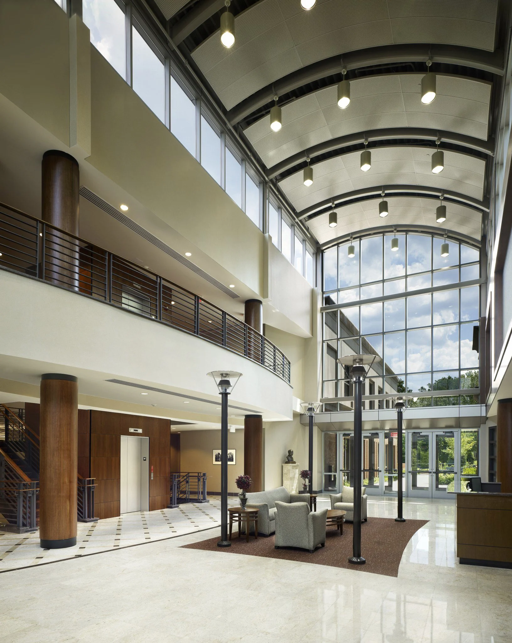 Interior lobby with seating area, marble floors, large glass windows, and high, curved ceiling with hanging lights.
