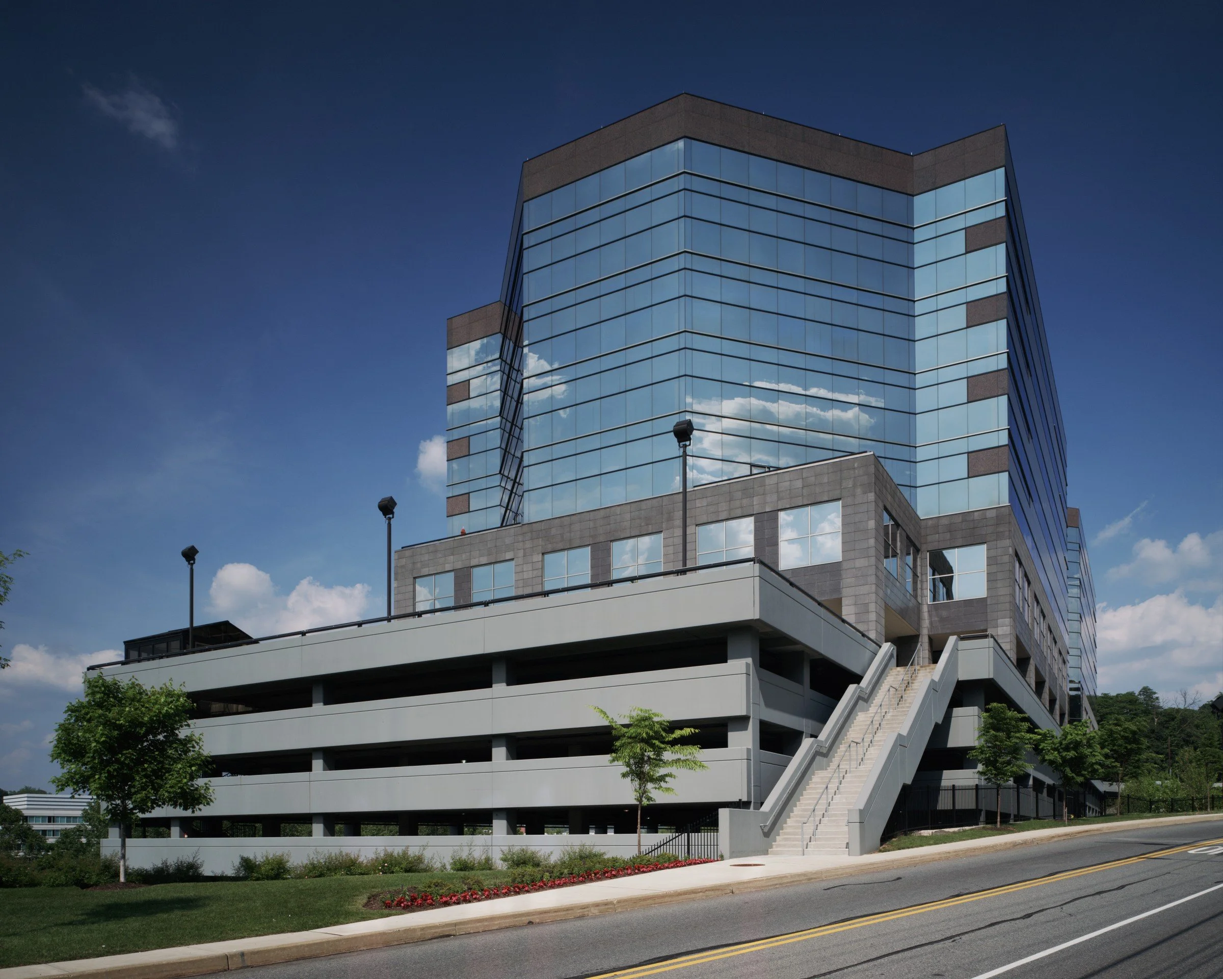 Modern glass and concrete office building with exterior staircase and landscaped yard under clear blue sky.