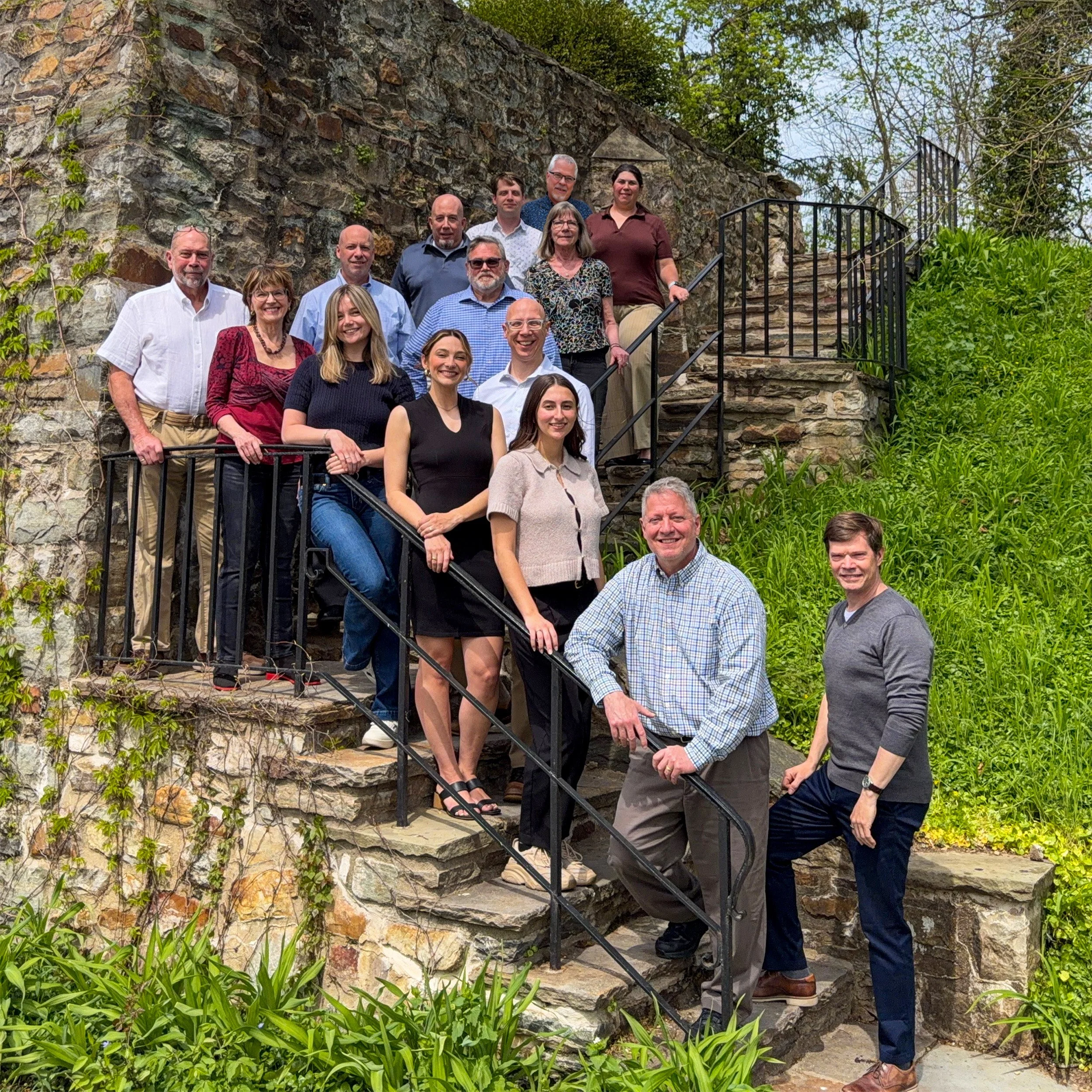 Architectural Concepts' team standing on a stone staircase outdoors, posing for a photo, with greenery and a stone wall in the background.