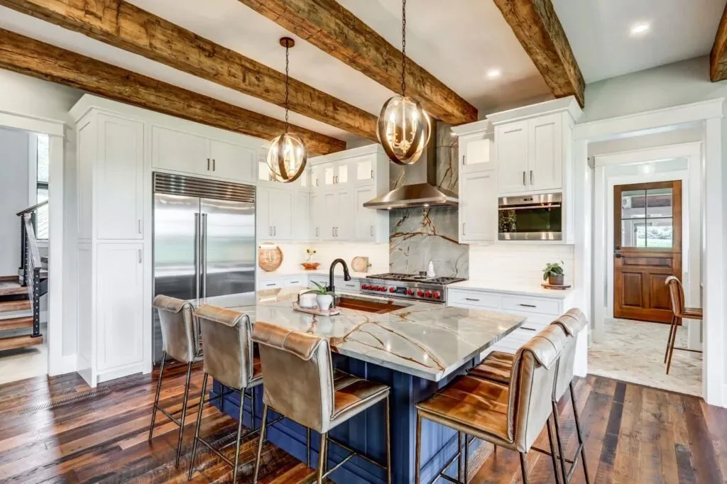 Modern kitchen with white cabinetry, wood beams on ceiling, marble island with seating, stainless steel appliances, and dark wood flooring.