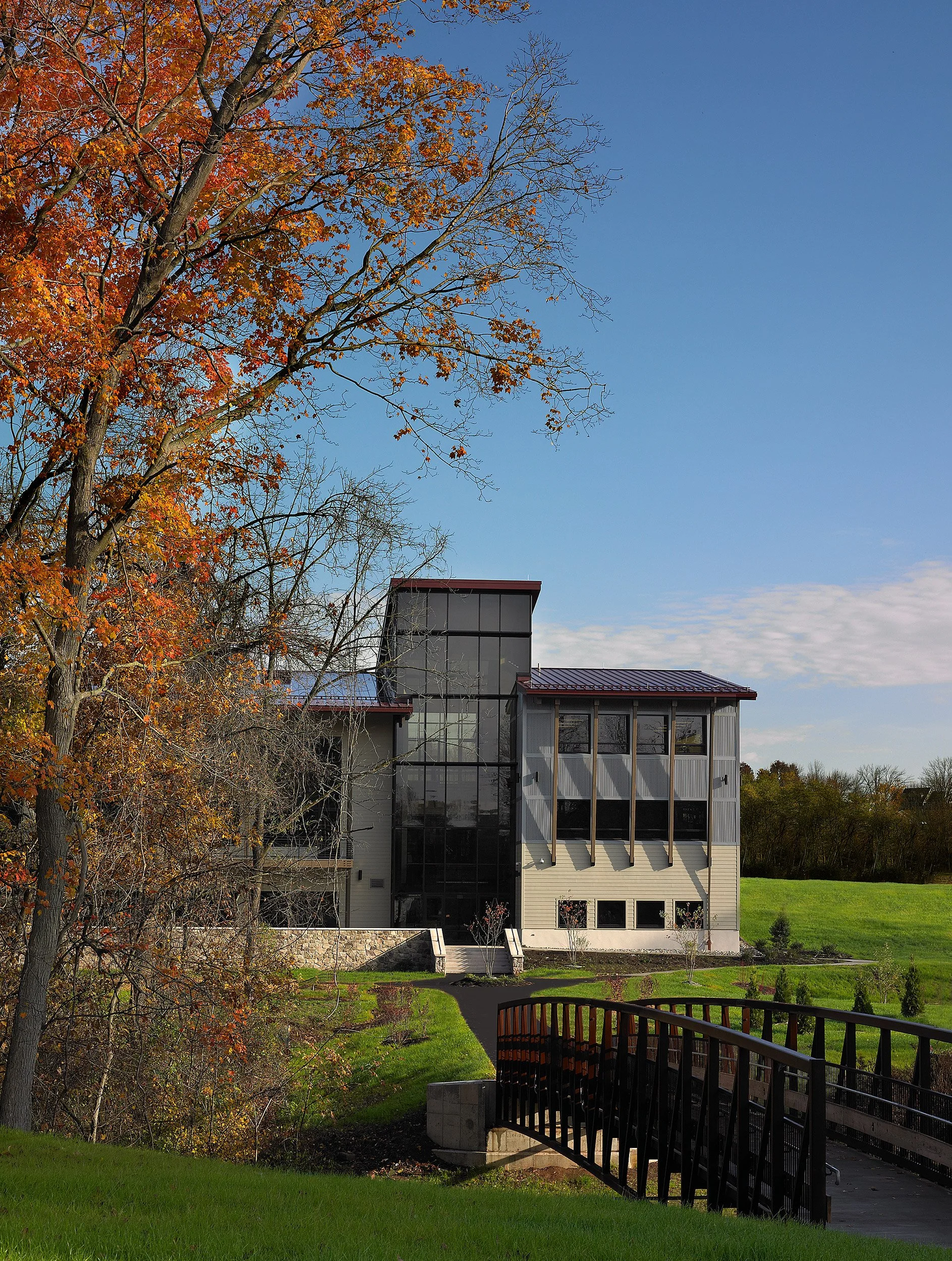 A modern conference center with large glass windows, surrounded by green grass and trees with autumn leaves, under a clear blue sky.