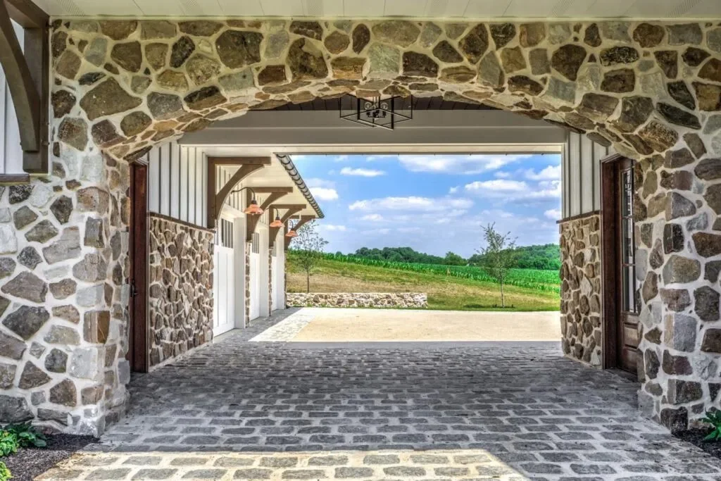 View of a stone archway leading to an open landscape with green fields and blue sky with clouds.