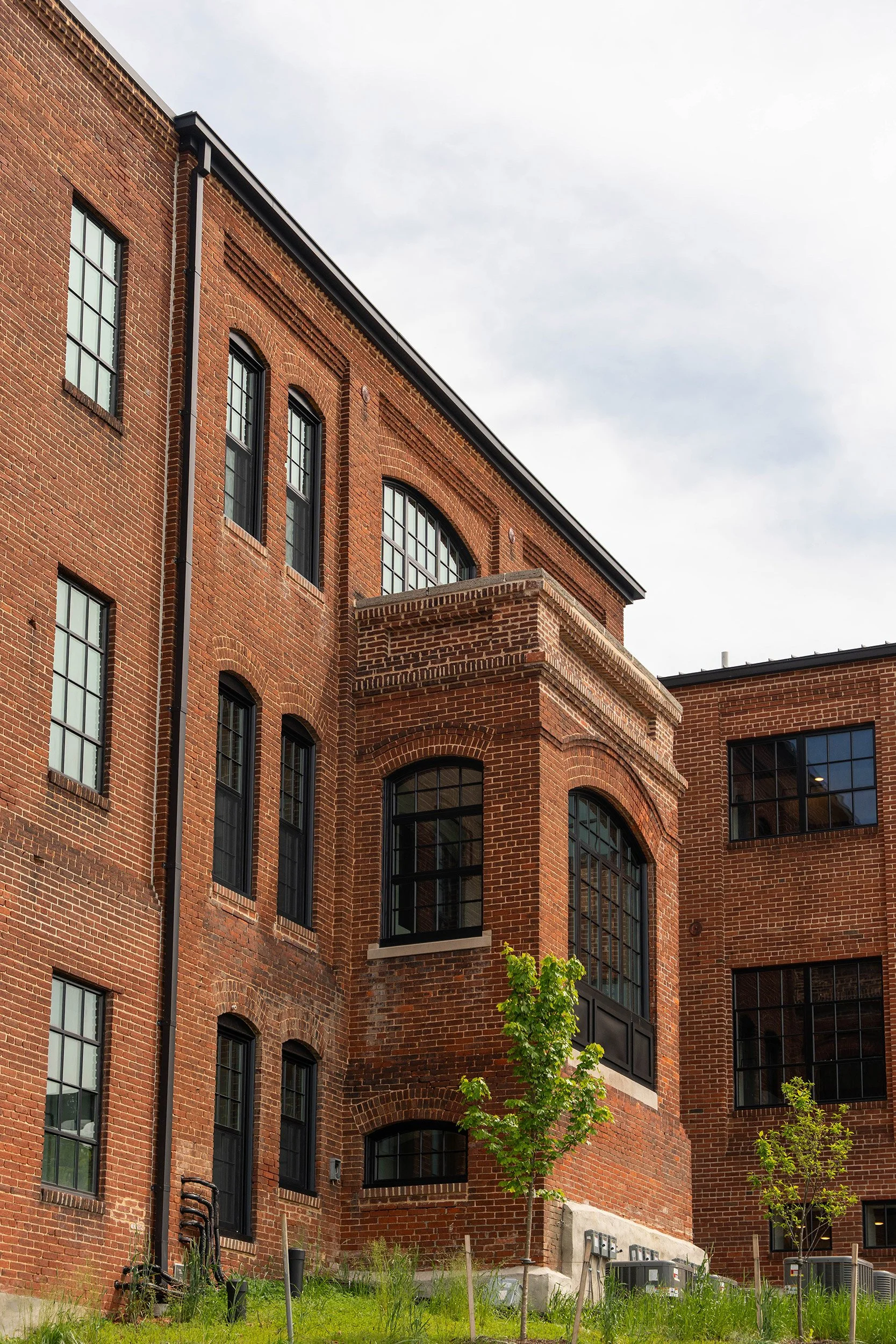 Red brick apartment building with large black window panes and small trees in front.