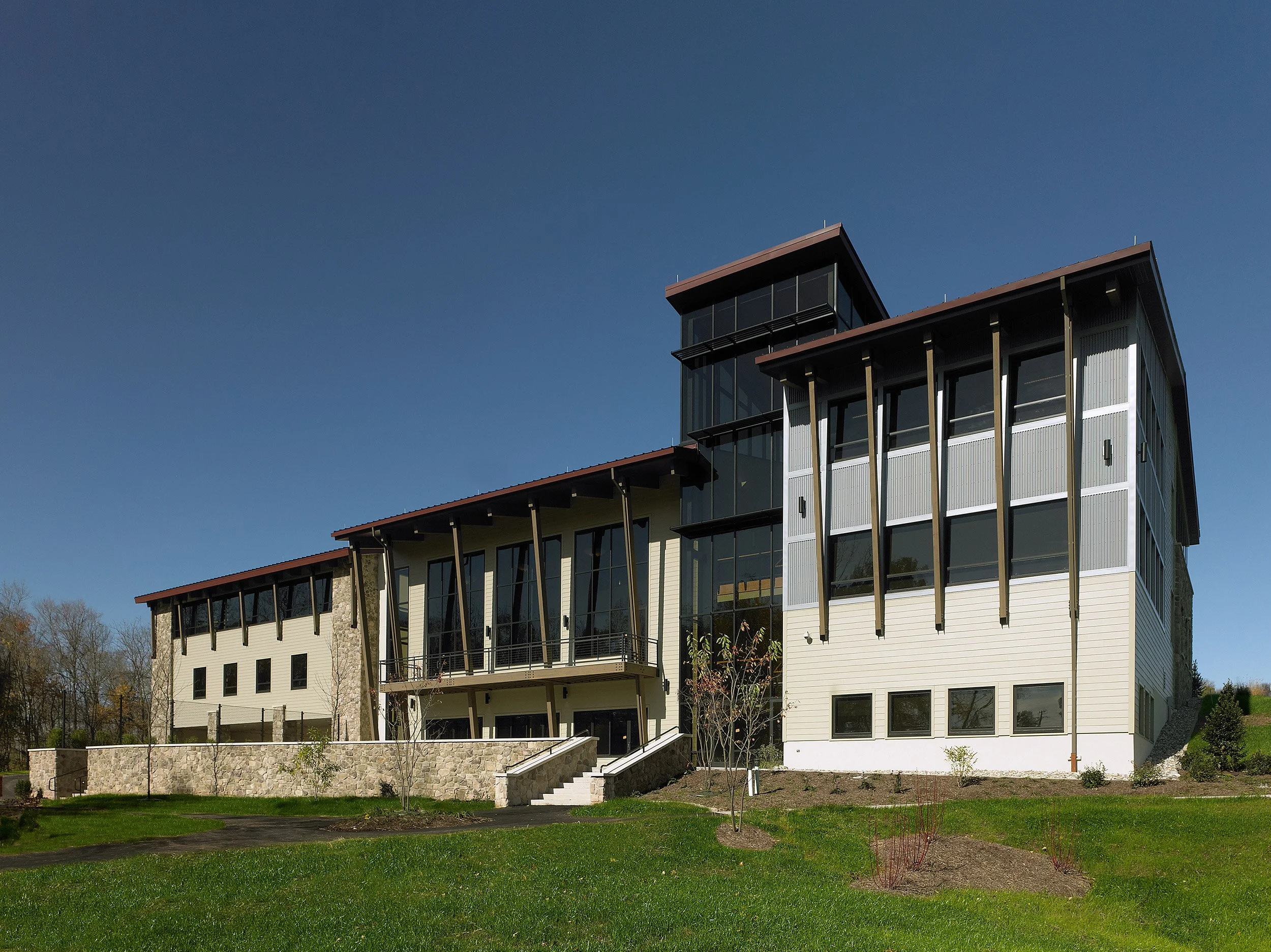 Modern multi-story conference center with large glass windows and angled architectural features, surrounded by green lawn and small trees.