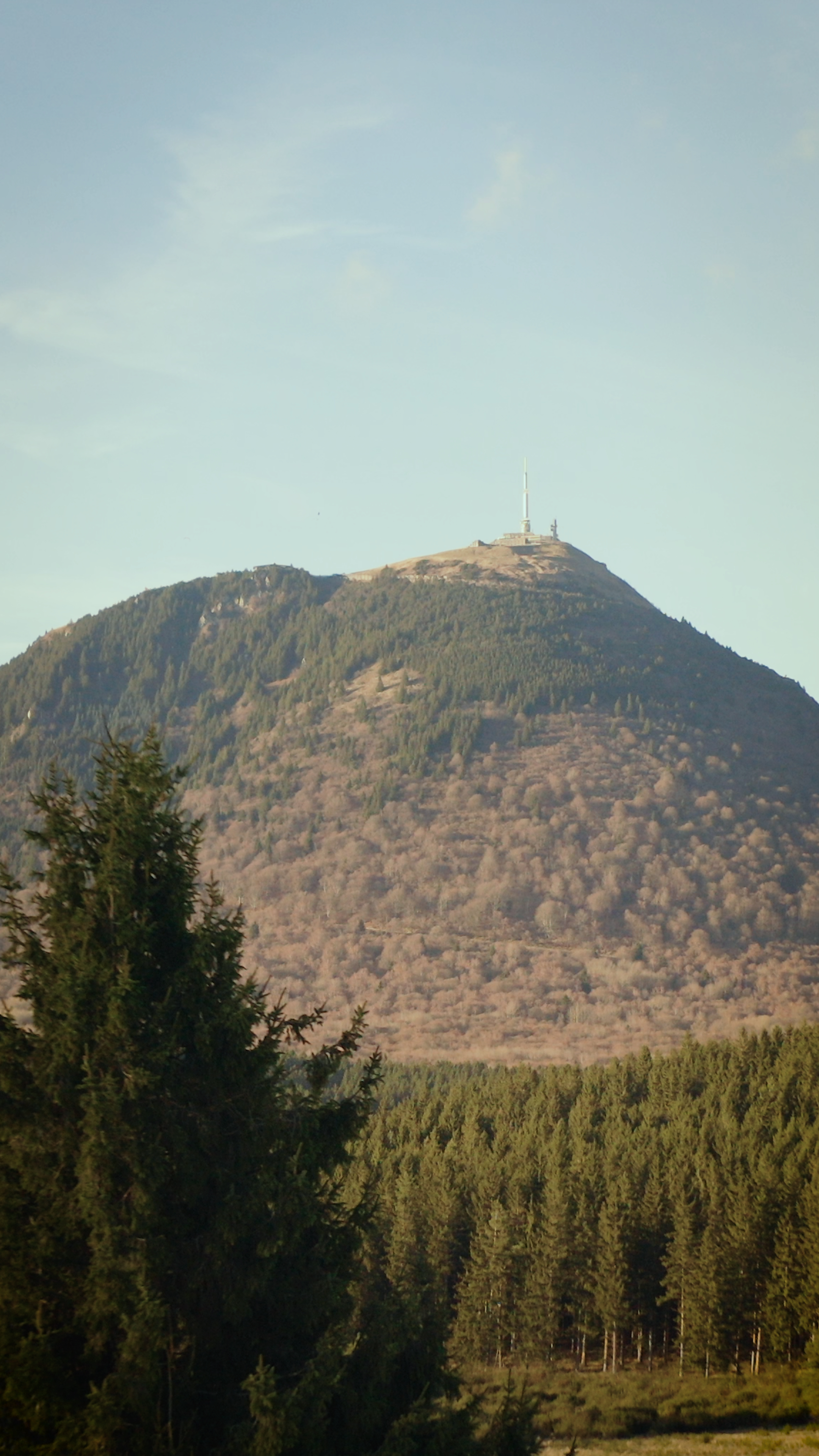 Montagne avec forêt dense en premier plan et sommet avec antenne et bâtiment au sommet.