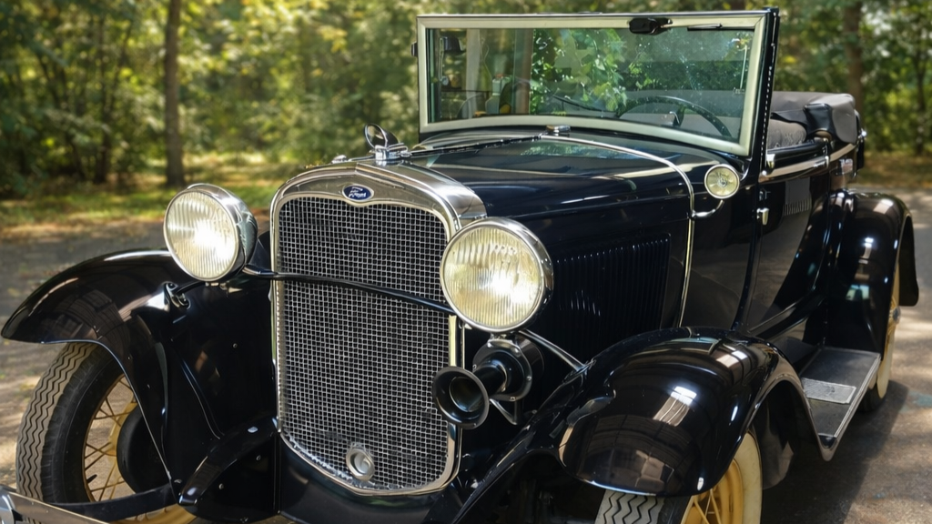 Vintage black convertible car parked outdoors with trees in the background.