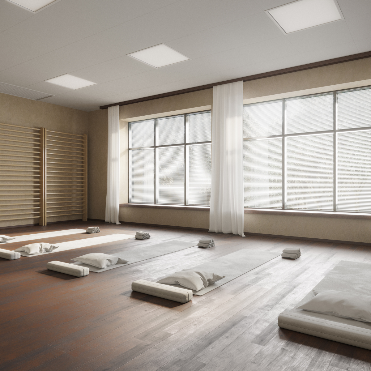 A bright, spacious yoga or meditation room with large windows, white curtains, and wooden floors. There are four yoga mats with pillows and rolled towels set up on the floor, indicating a preparation for a class or session.
