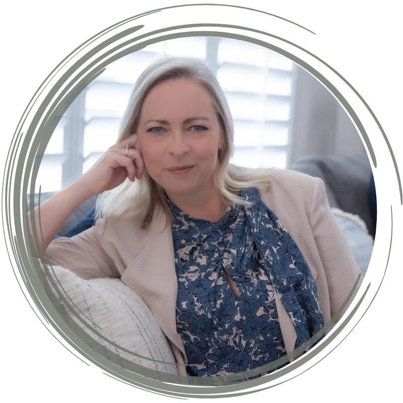 A woman with blonde hair sitting on a couch in a well-lit room, wearing a beige blazer and a navy floral blouse, with a confident expression.