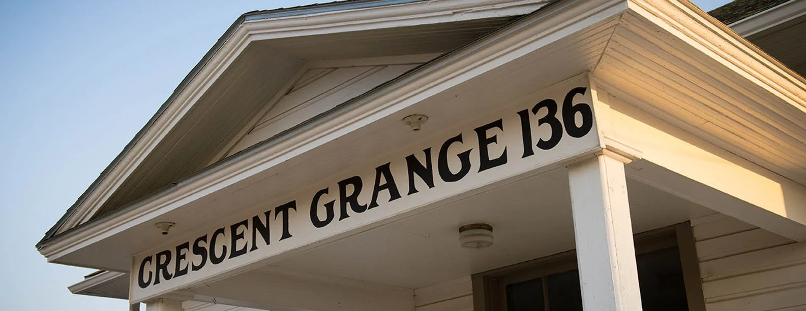 Close-up of a house's front porch with a white sign that reads 'CRESCENT GRANGE 136 in black letters, under a gabled roof.