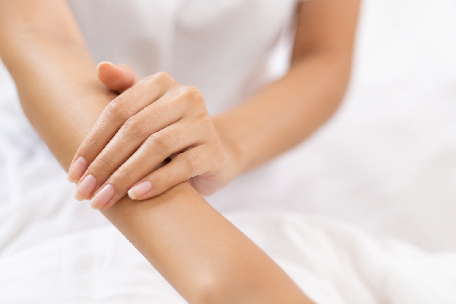 A person with light skin is holding their arm, which is being gently touched by the other hand.