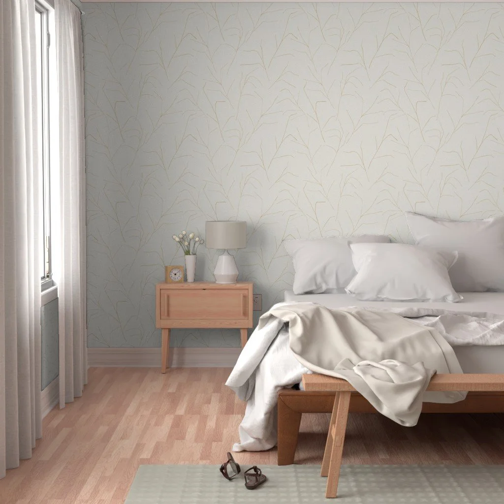 A bedroom with a bed, white pillows, and linen. Wallpaper is a cream color, with gold textural, minimalist lines. There's a small wooden nightstand with a white lamp, a small clock, and a vase with flowers.