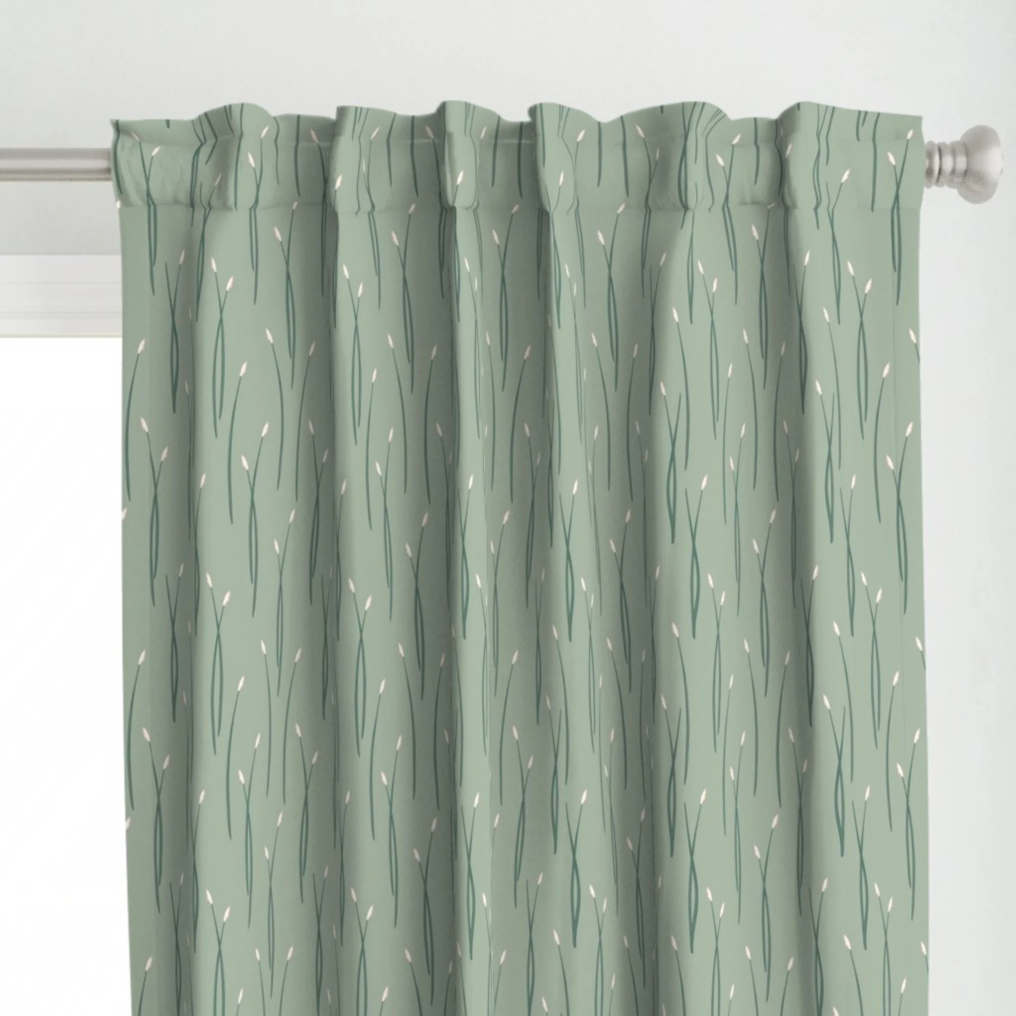 A close-up of a curtain with a light green color and a pattern of dark green skinny reed grasses, with white accents, hanging from a white curtain rod in front of a white wall.