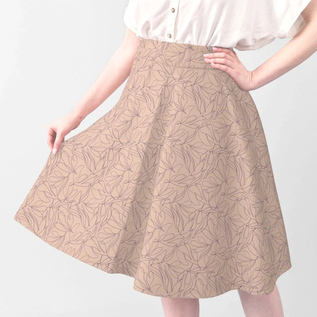 Person wearing a peachy pink skirt with a leaf linework pattern, pairing it with a white blouse, standing against a plain light background.