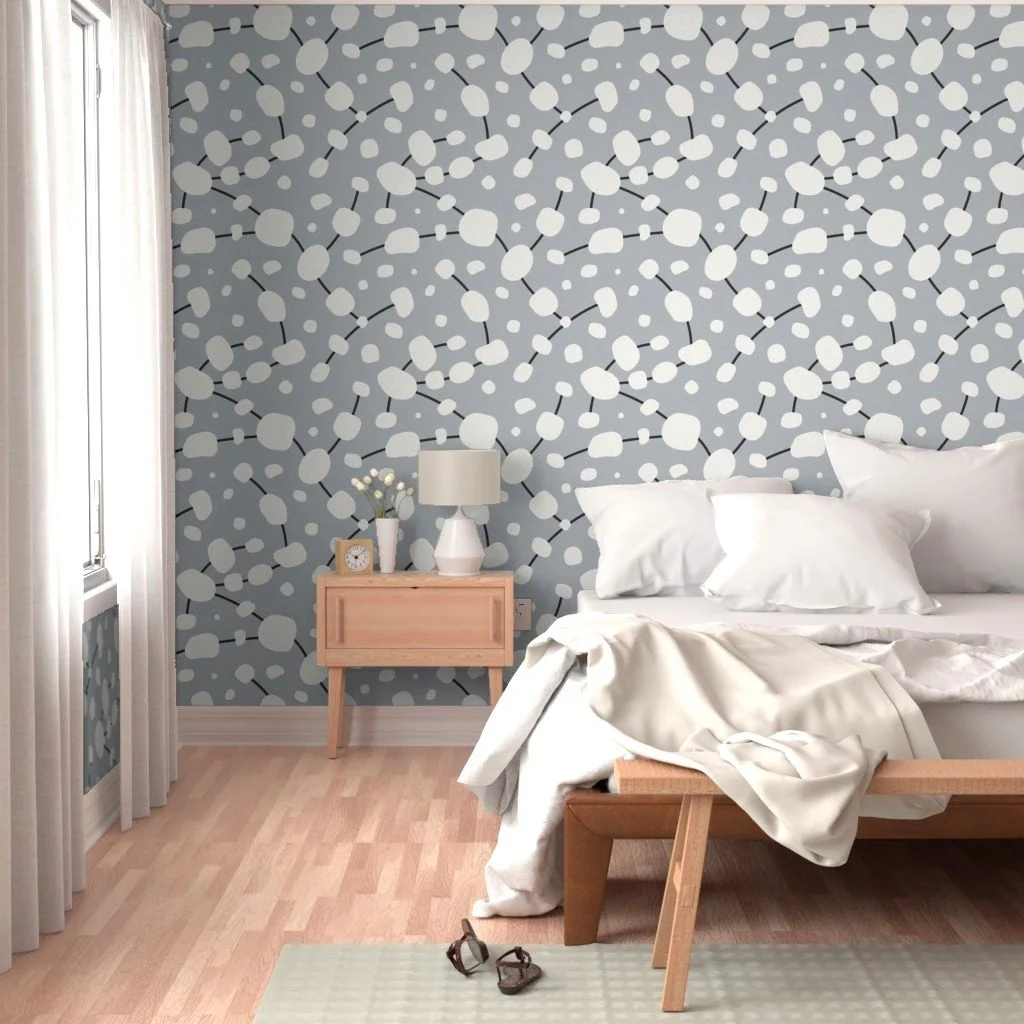 Large-scale seamless repeating design, with cream organic stone shapes with charcoal connecting lines, shown on wallpaper in a bedroom setting.