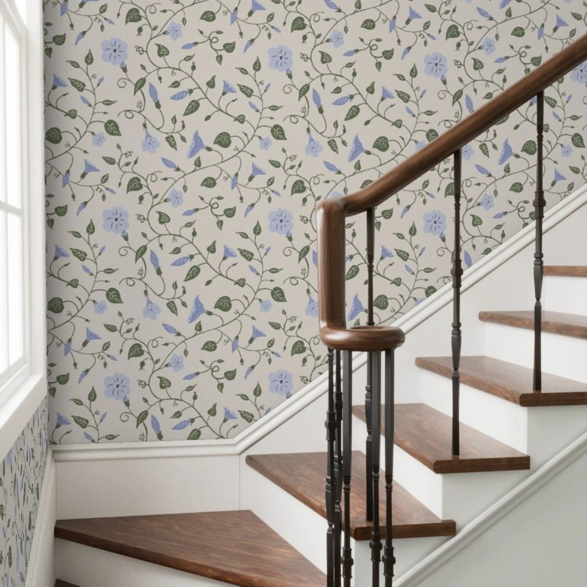A staircase with wooden steps and black metal balusters ascending alongside a wall with floral wallpaper featuring blue flowers and green leaves on a cream background.