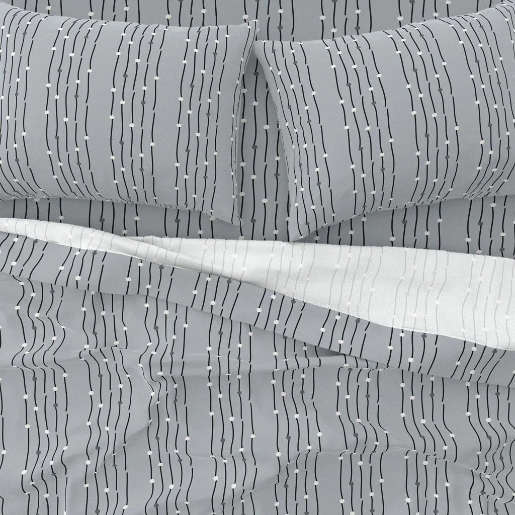 Close-up of bed sheets and pillows with a gray and white striped pattern, featuring small white dots on the stripes.