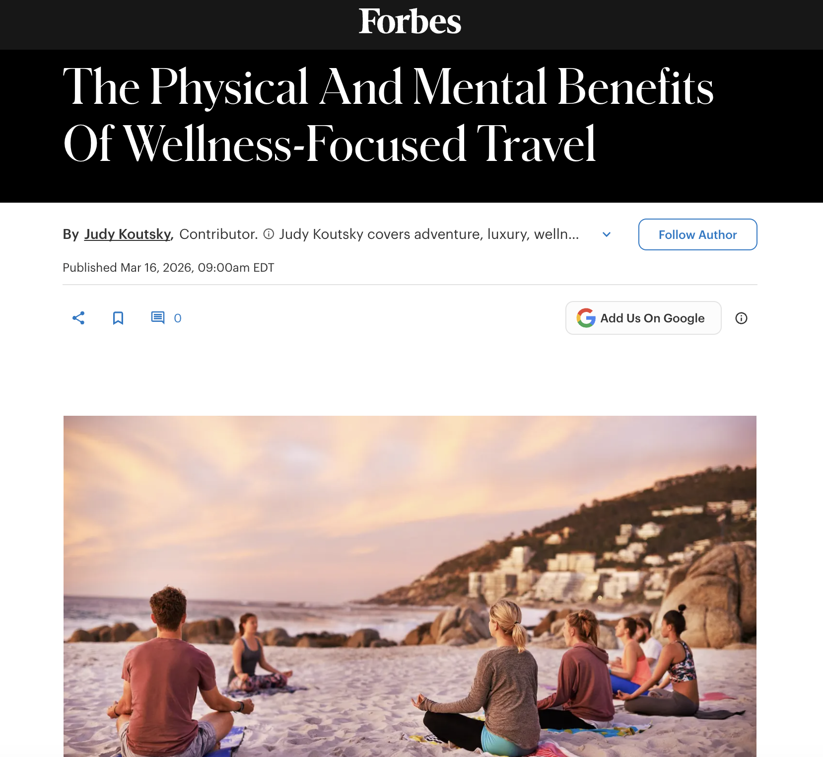 Group of people practicing yoga on the beach at sunset, with rocky hills and buildings in the background.