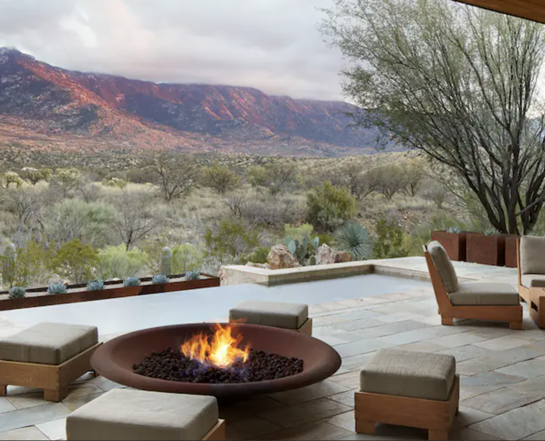 Outdoor patio with a fire pit and seating, overlooking a scenic desert landscape with mountain ranges and sparse vegetation.