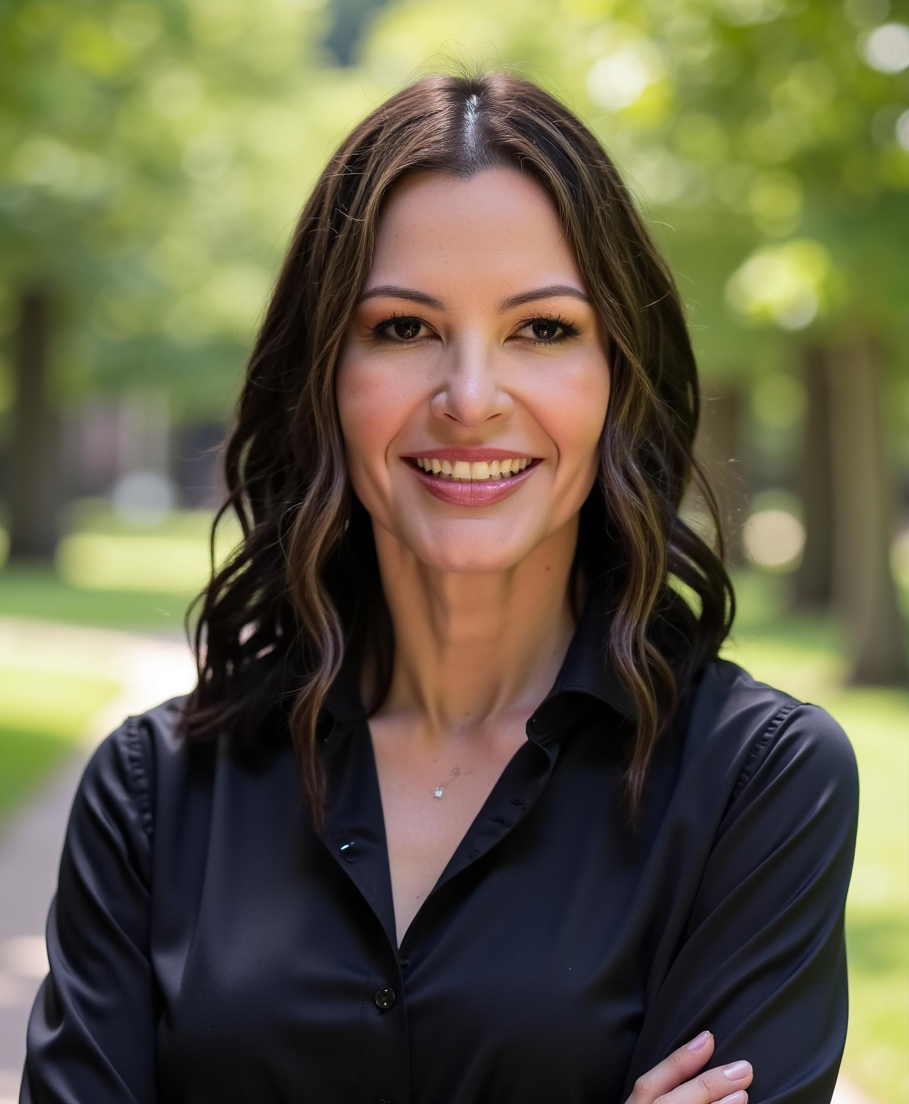 Ivette Diaz smiling outdoors with blurred green trees in the background, wearing a black button-up shirt.