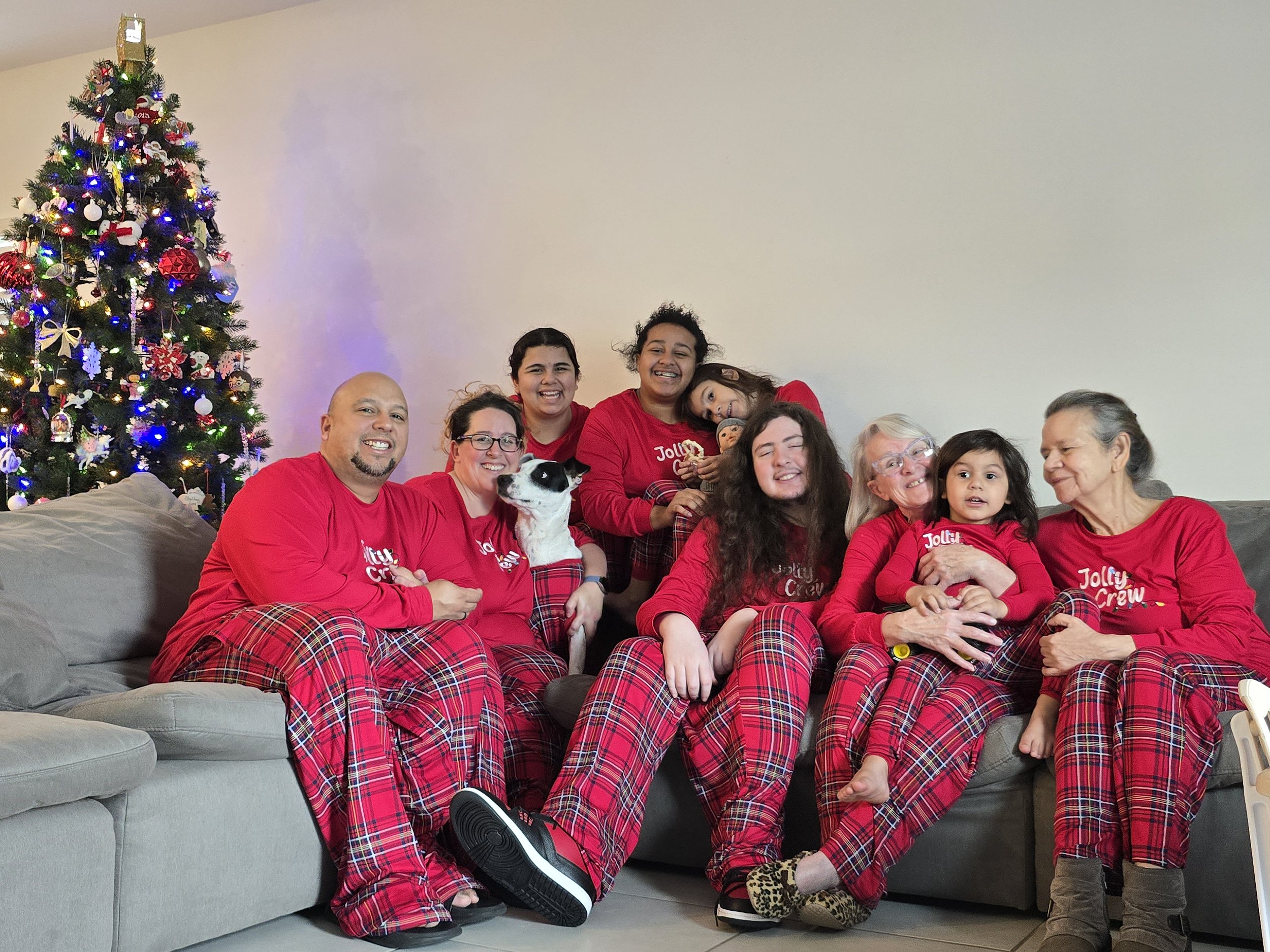 Family of Fun Media family wearing matching red holiday pajamas, sitting together on a couch with a Christmas tree, celebrating together.