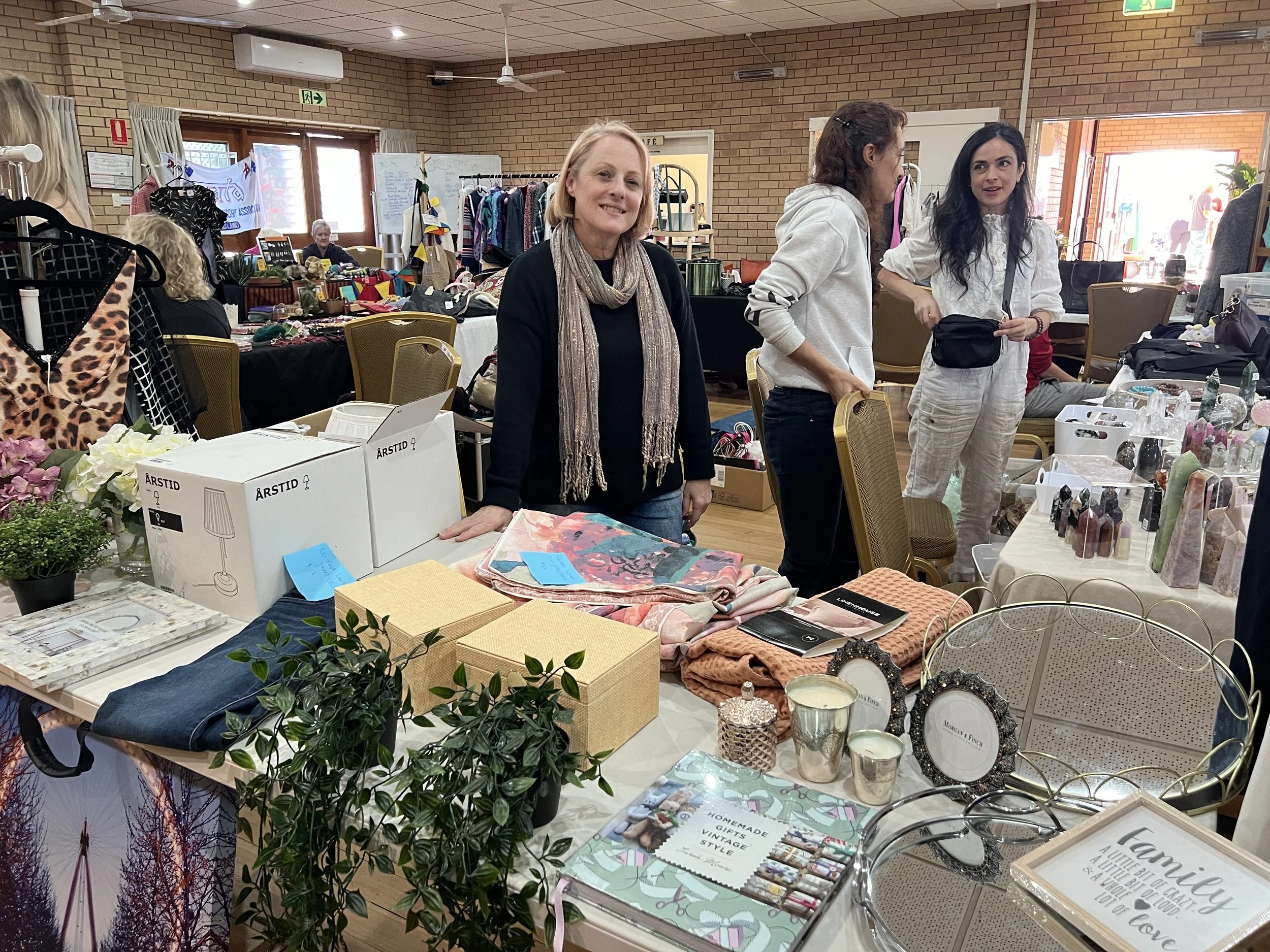 People browsing at a market stall filled with household items, decor, and gifts amid a cozy indoor setting with brick walls.