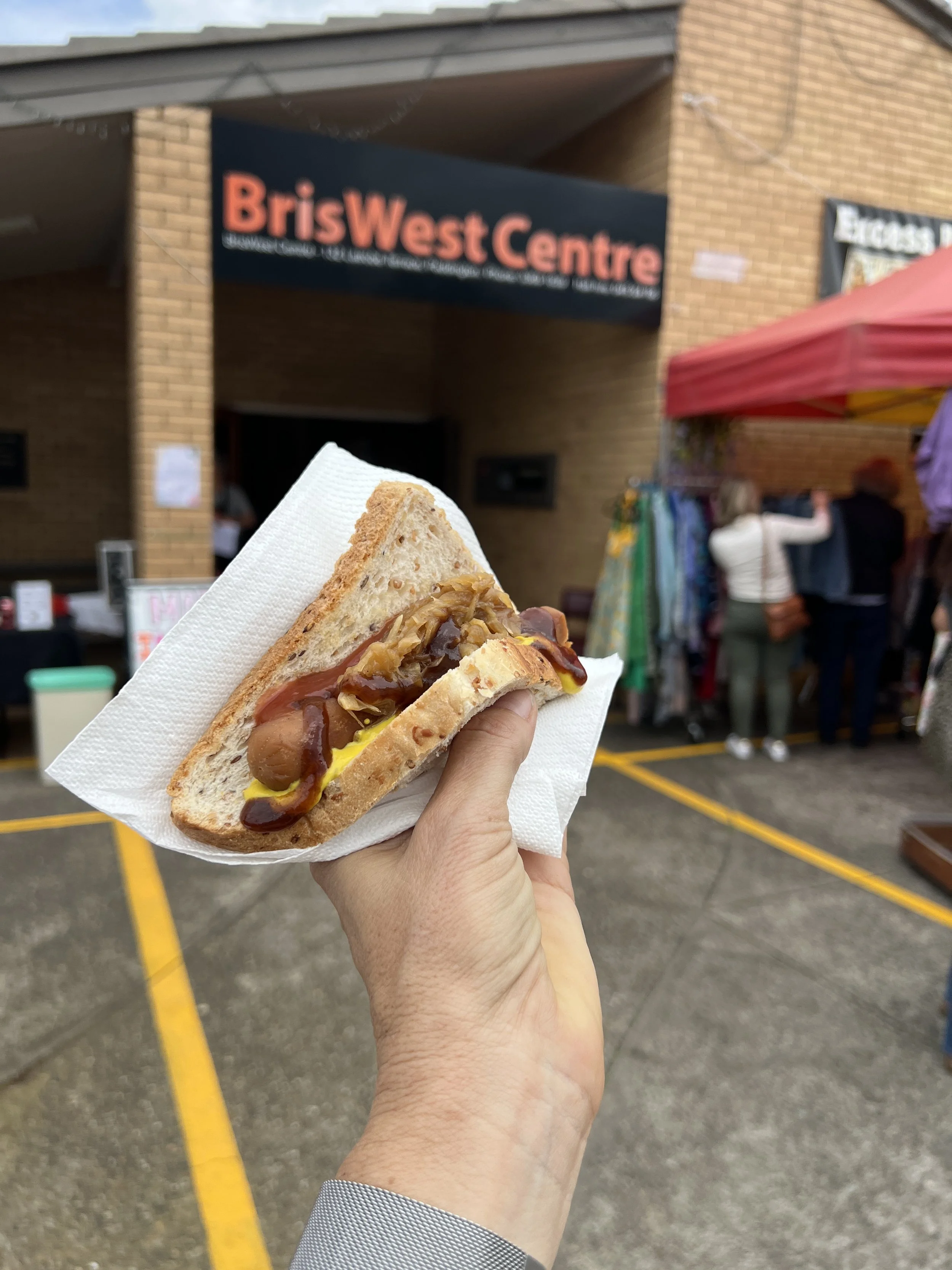 A hand holding a sausage with sauce in bread and a napkin.