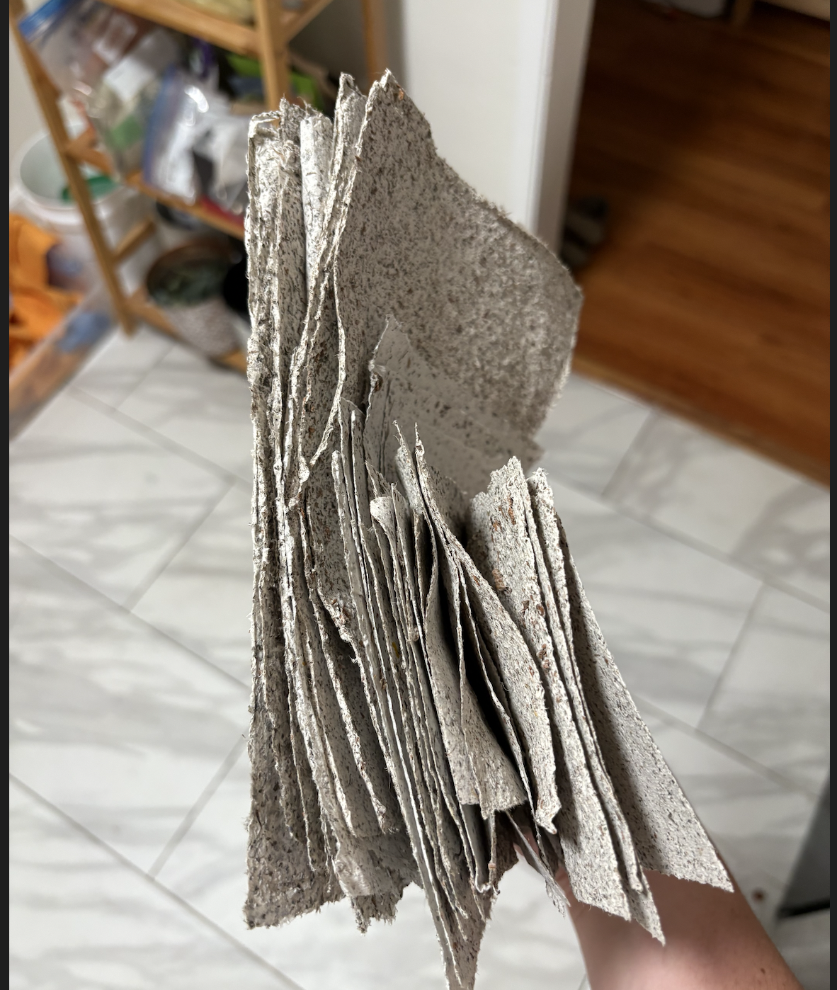 A close-up view of a stack of rough, textured gray stones or tiles held in hand indoors.