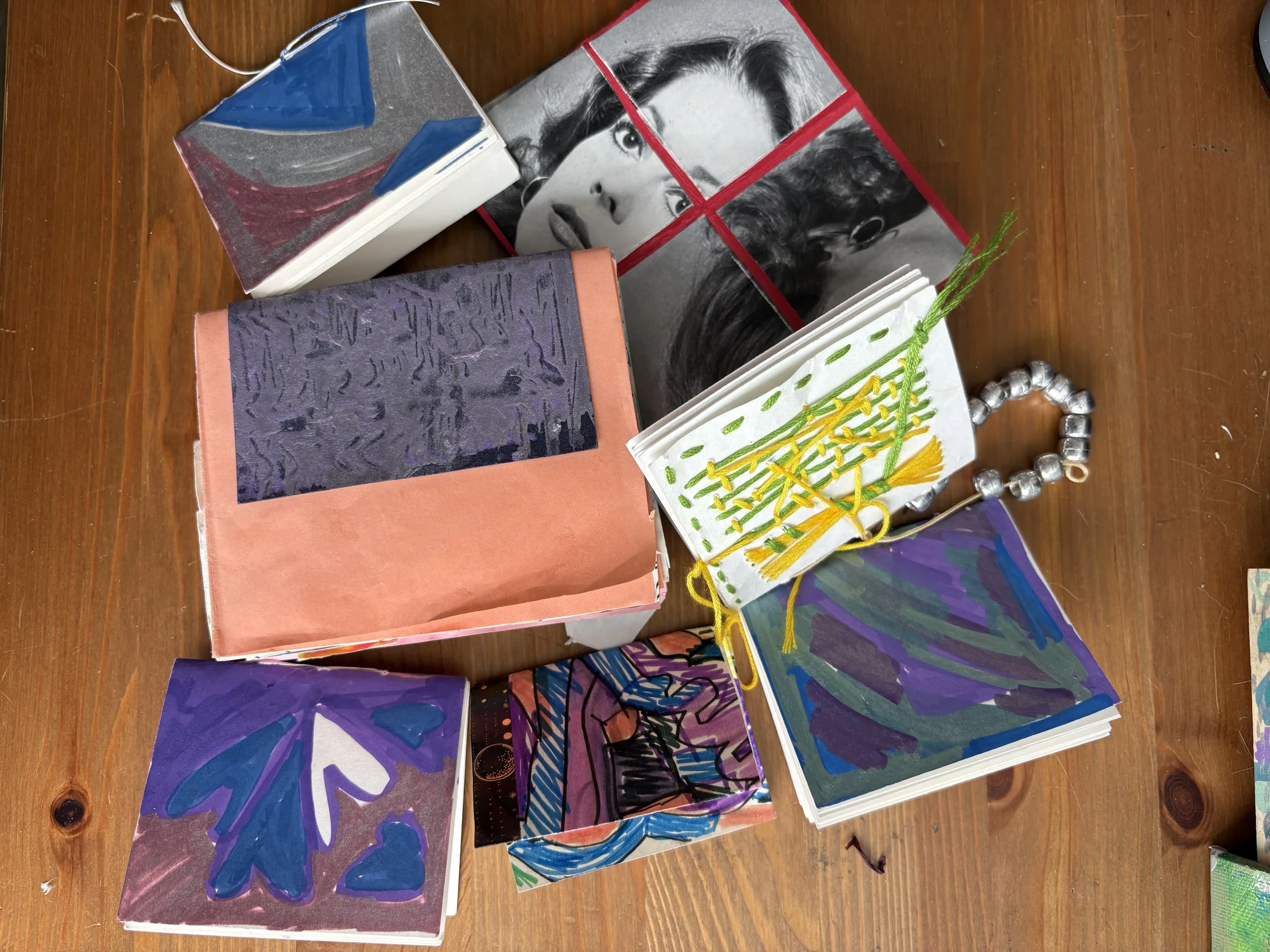 Collection of handmade art books and embroidered items on a wooden surface, including some with painted and stitched images and patterns.