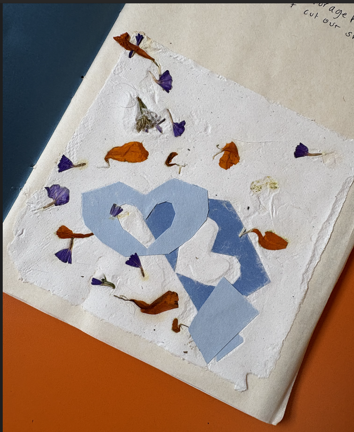 A piece of textured white paper with dried purple, orange, and yellow flowers, and cut-out blue paper hearts.