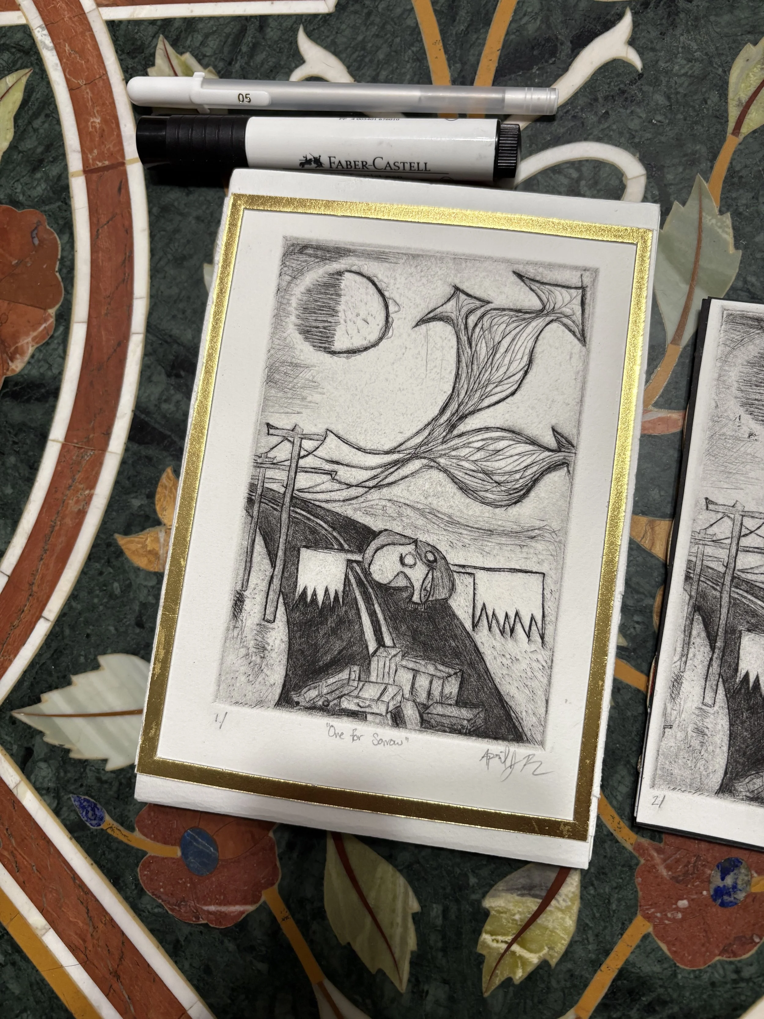 A pencil sketch on paper featuring a moon in the sky, wind-blown trees, and a skull resting on a pile of boxes, with a bridge or platform in the background. The sketch is titled 'One for Sons'.