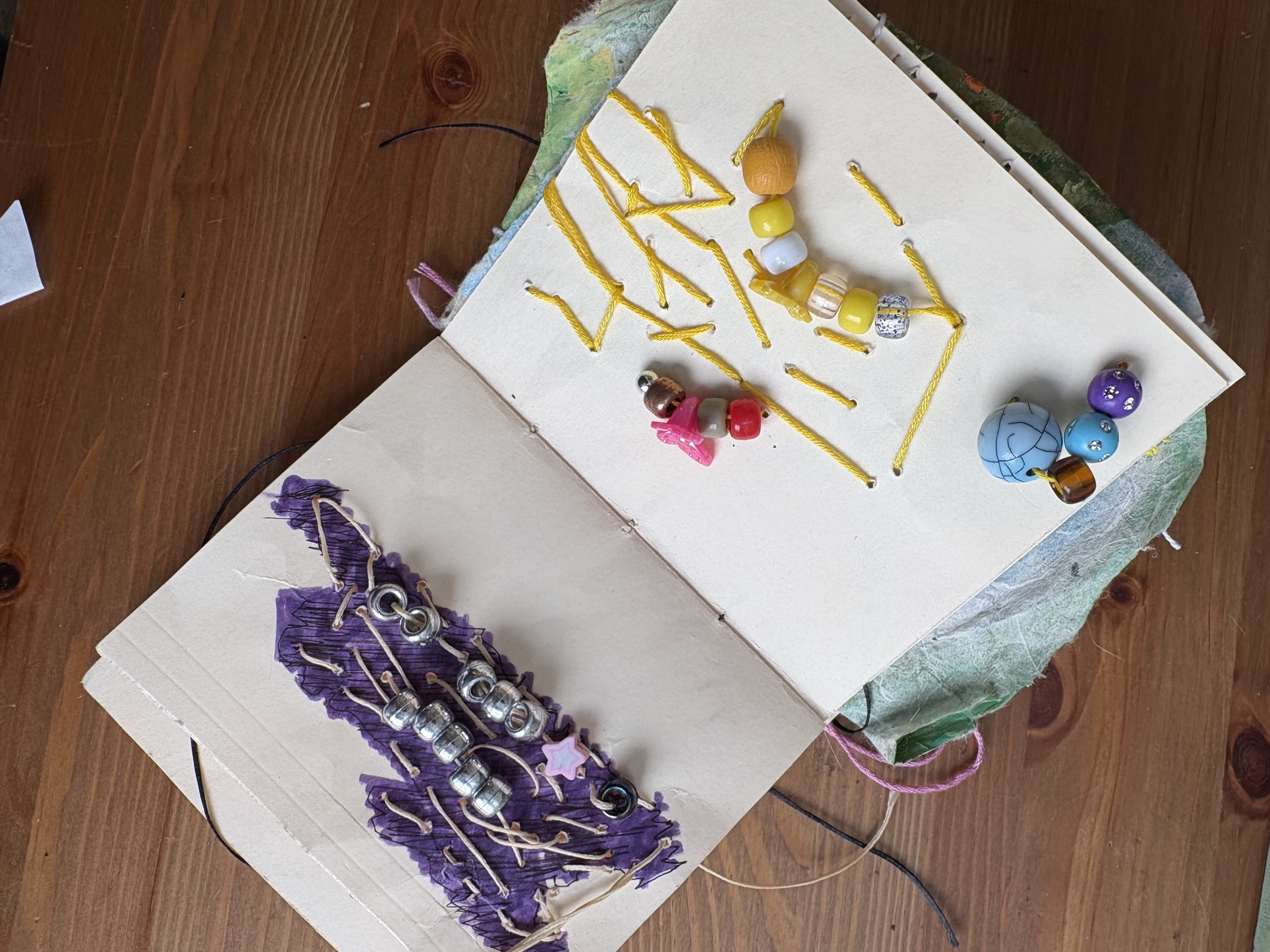 Open craft book with beads, buttons, and decorative items for jewelry making and craft projects on a wooden table.