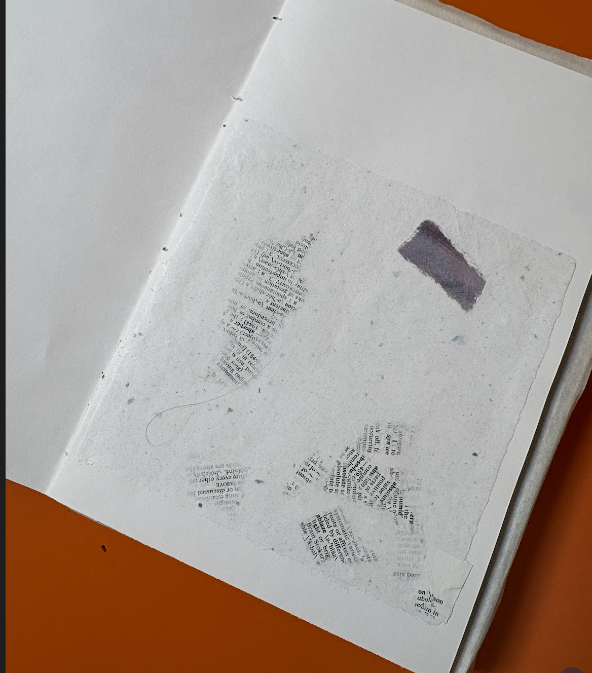 Open book with textured pages, featuring cut-out and torn sections with printed text, lying on an orange surface.