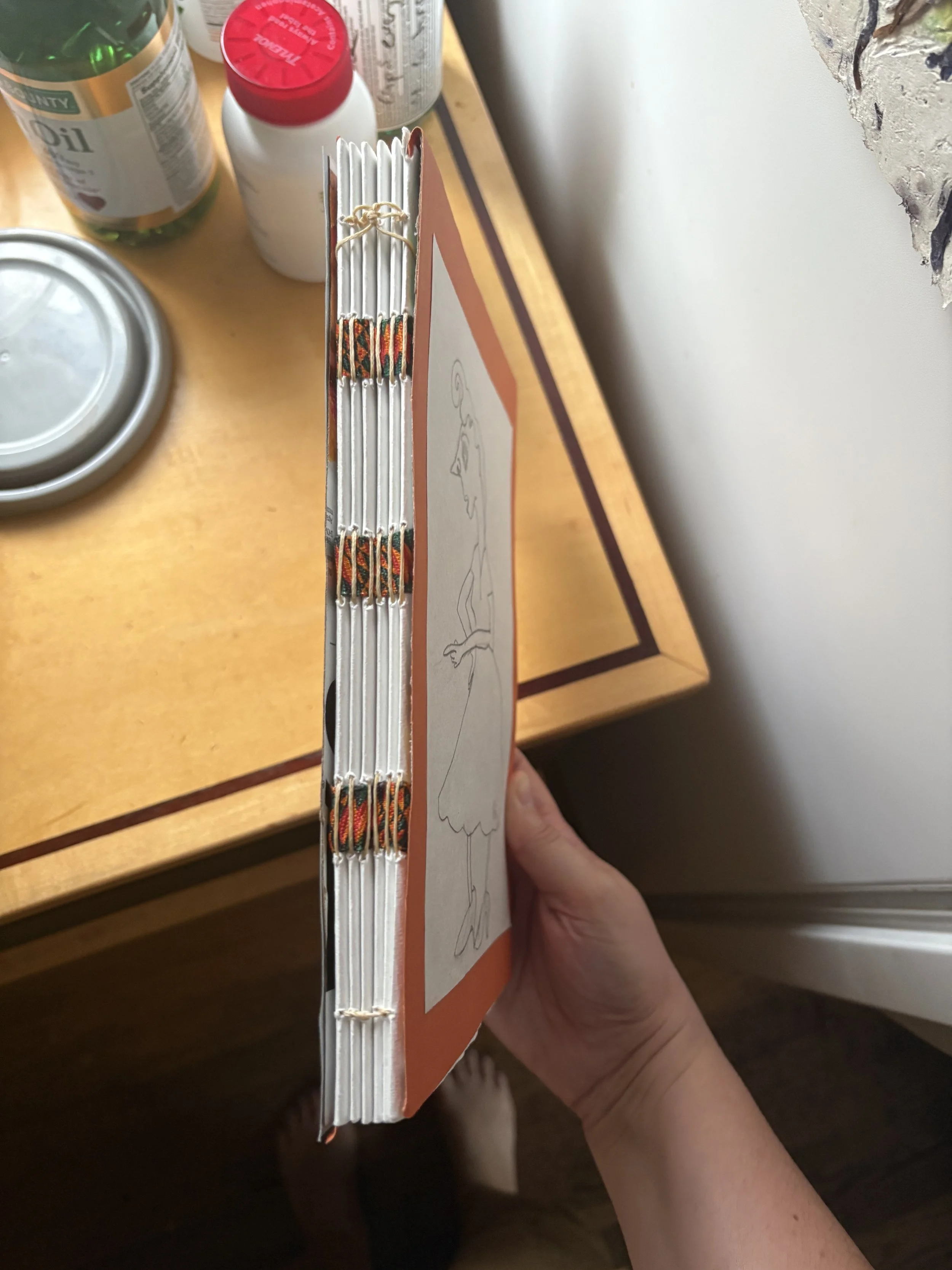 Side view of a cardboard box with wrapped wires on top, held by a person's hand above a wooden table with bottles and cans.