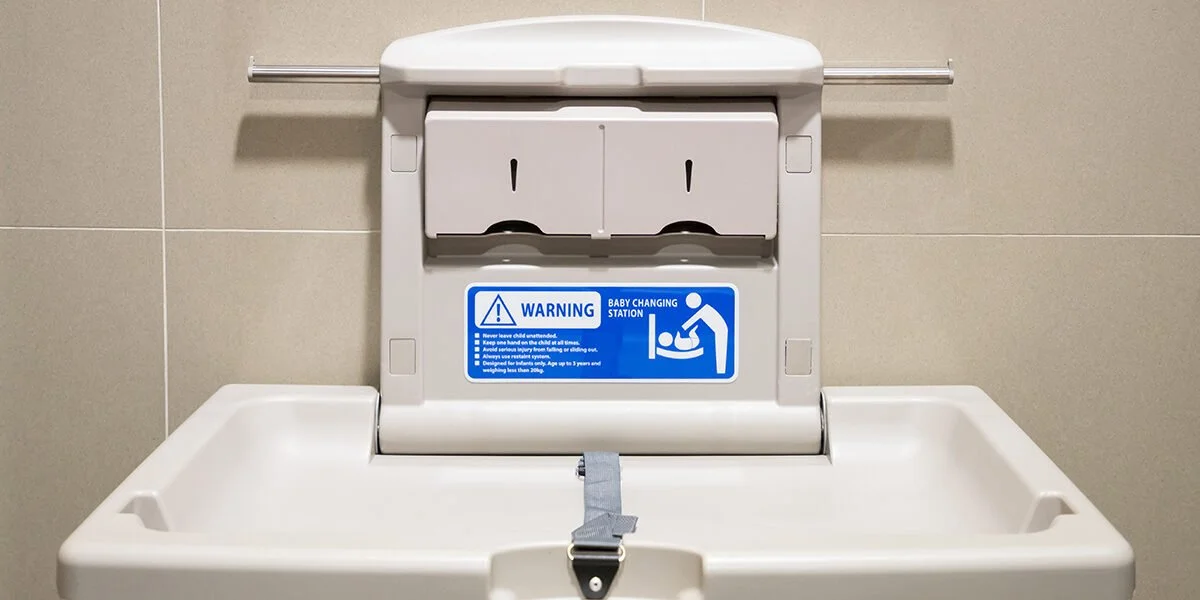 Baby changing station in a public restroom with a warning sign.