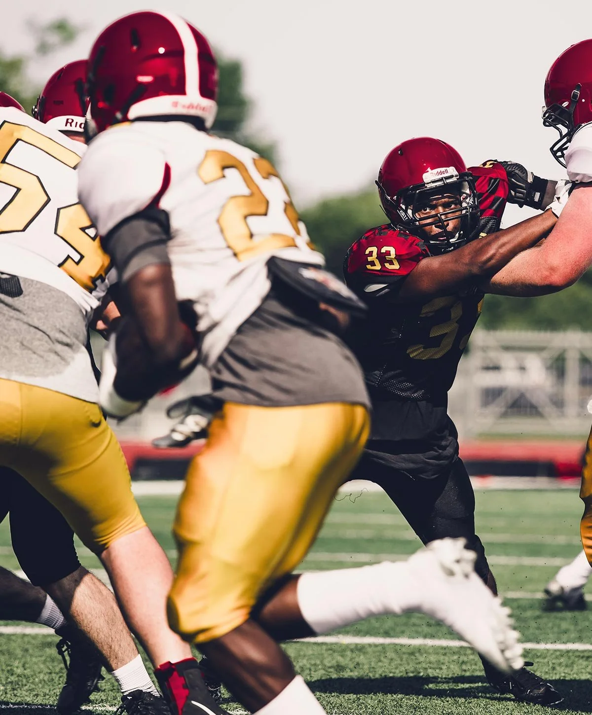 American football players in action during a game, with one player attempting to block or tackle and others engaged in the play, on a green field under an overcast sky.