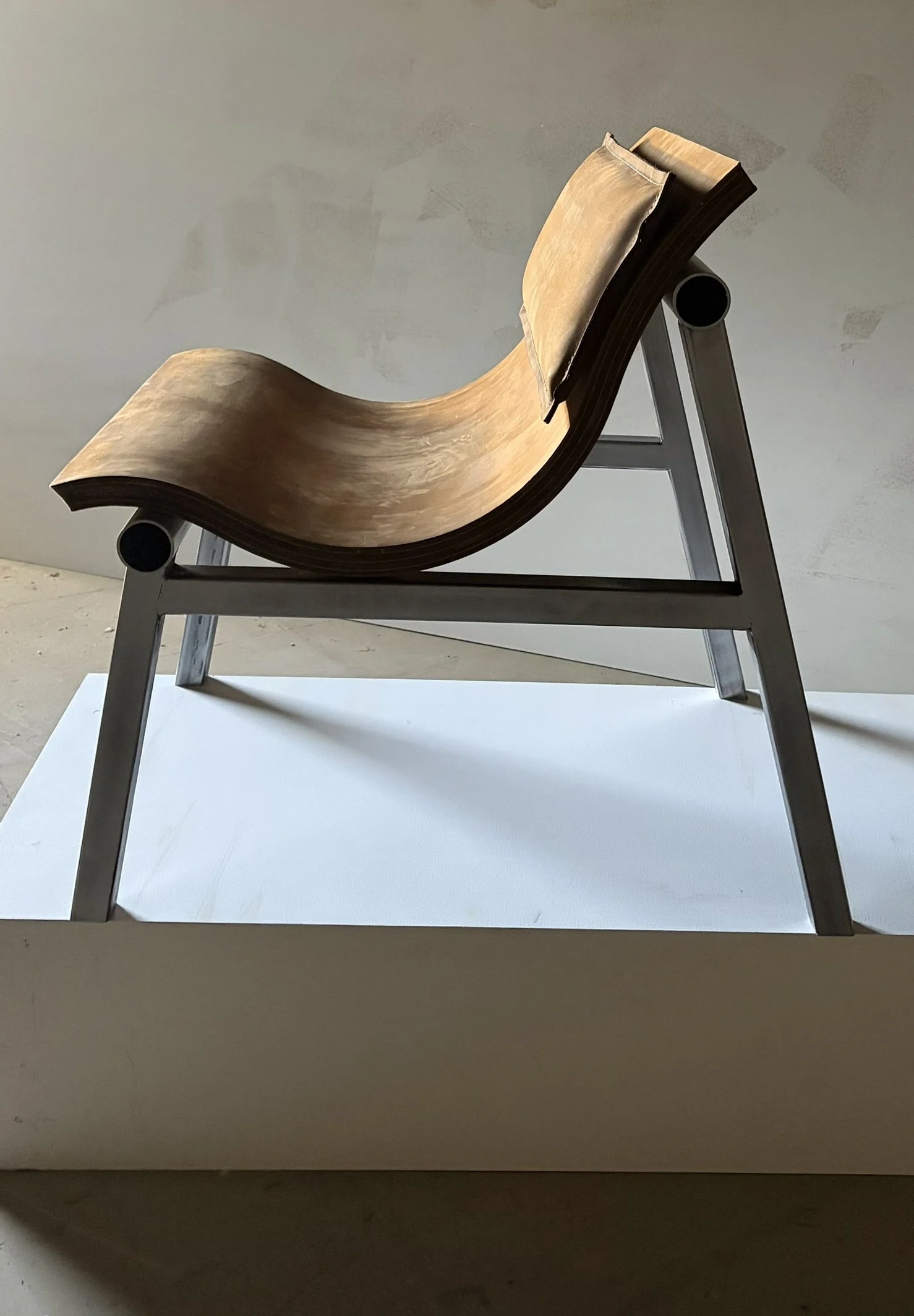 Modern chair with a curved wooden seat and metal frame, displayed on a white platform.