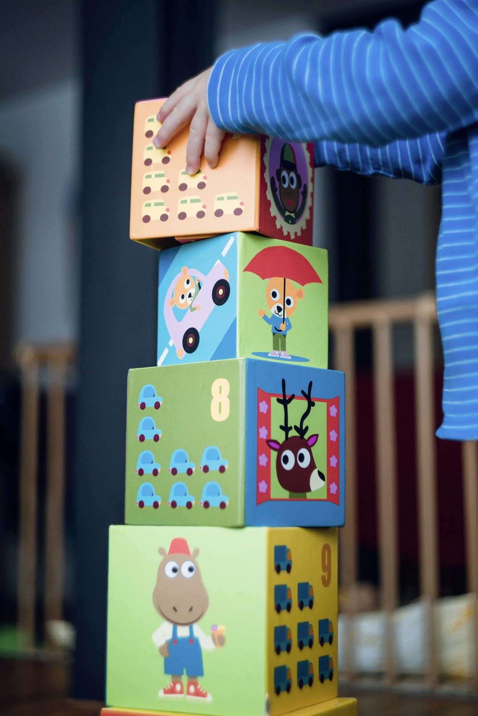 Child stacking colorful illustrated blocks with animals, cars, and numbers.
